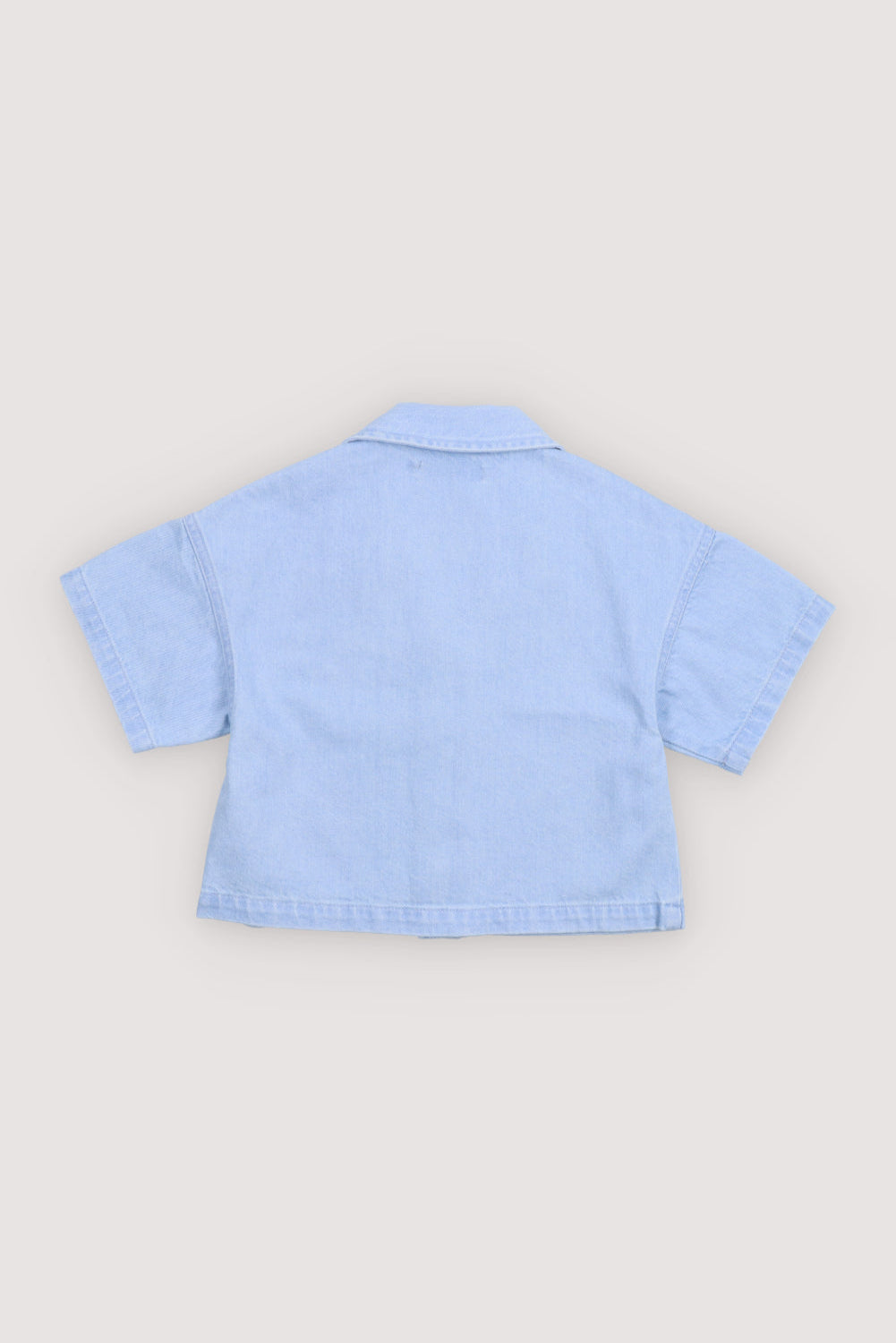 Short sleeve cropped shirt in washed denim, featuring a front snap closure, chest pocket, and TNS heart embroidery.