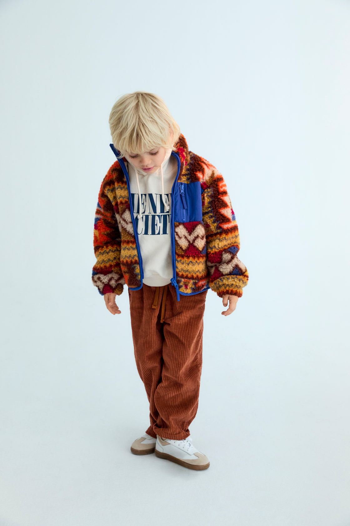 Child wearing a colorful jacket and brown pants on a white background