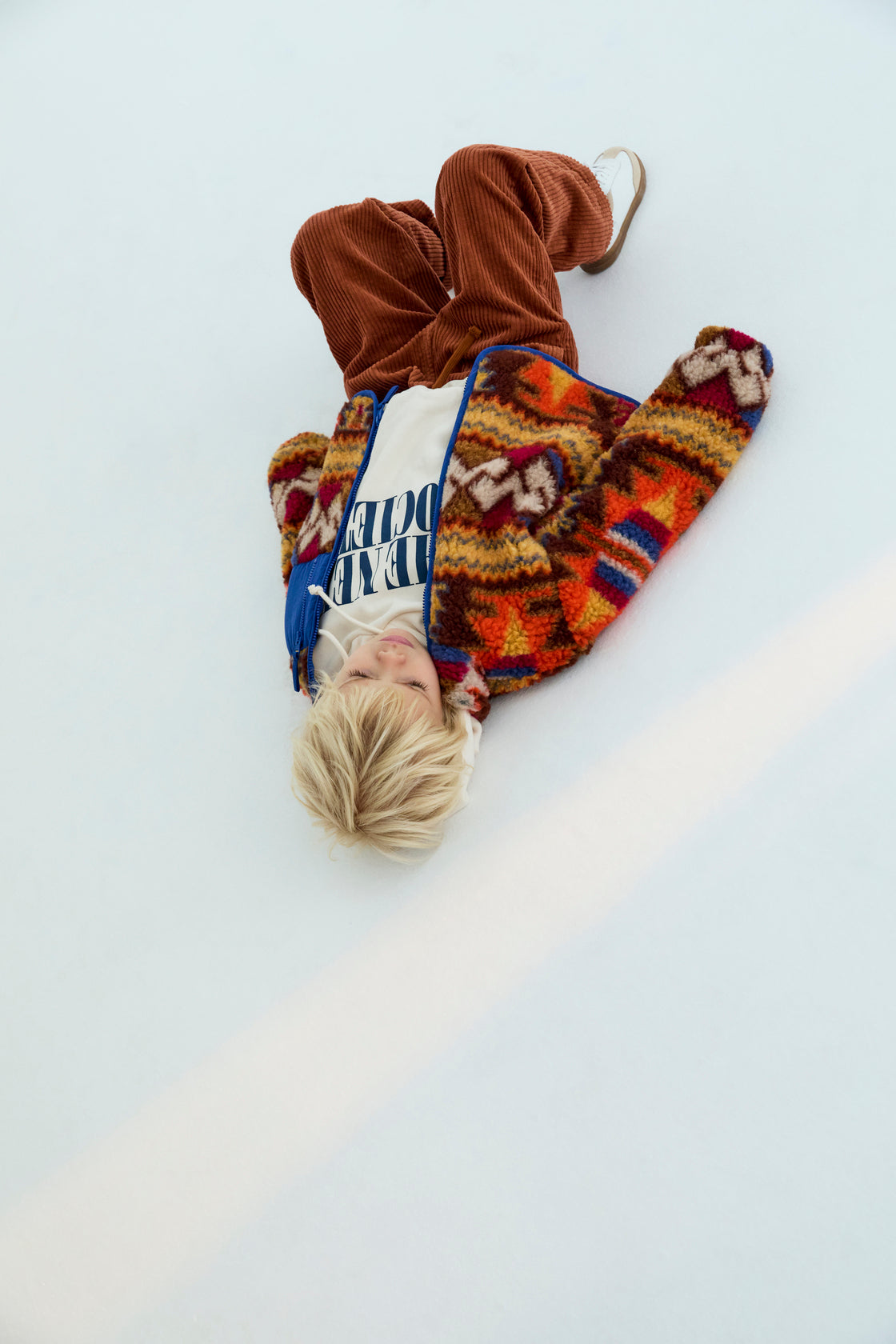 Person wearing a colorful patterned coat and brown pants on a white background