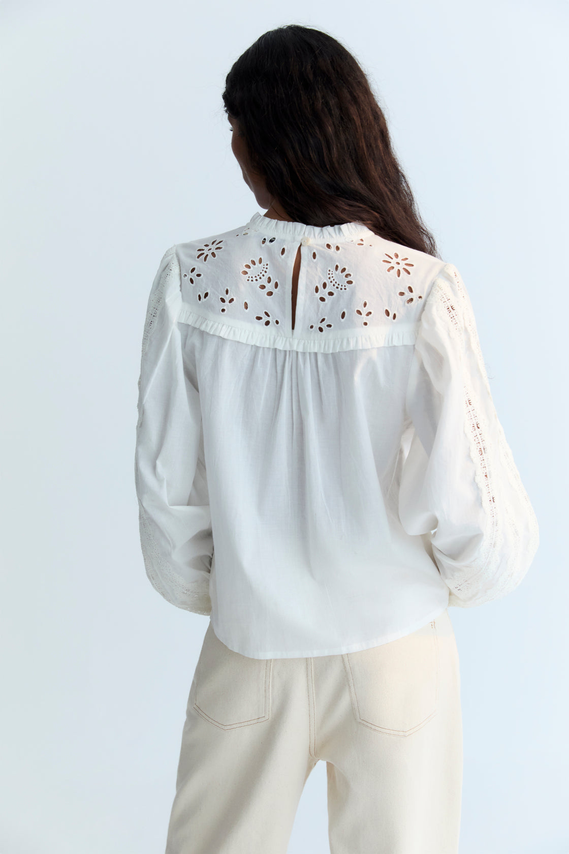 Cambric blouse with embroidered yoke detail and ruffles, and lace detailing on the body and sleeves. It features a back keyhole opening with a tone-on-tone button.
