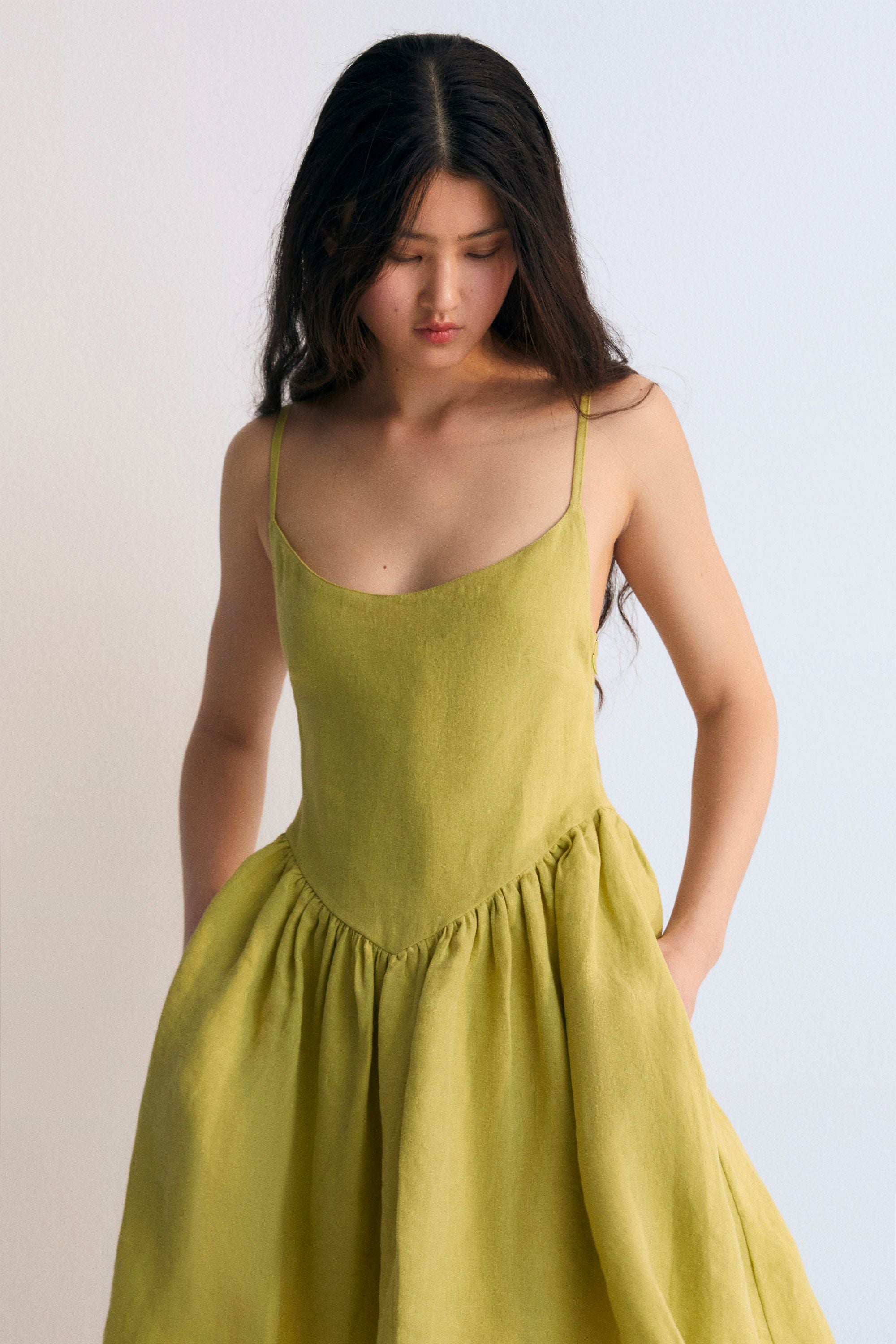 Hera Woman Short Dress in 100% linen, available in three colors: caviar, macadamia, and palm. Square neckline, straps with fasteners, and a short skirt with volume. Spring Summer Collection. The New Society.