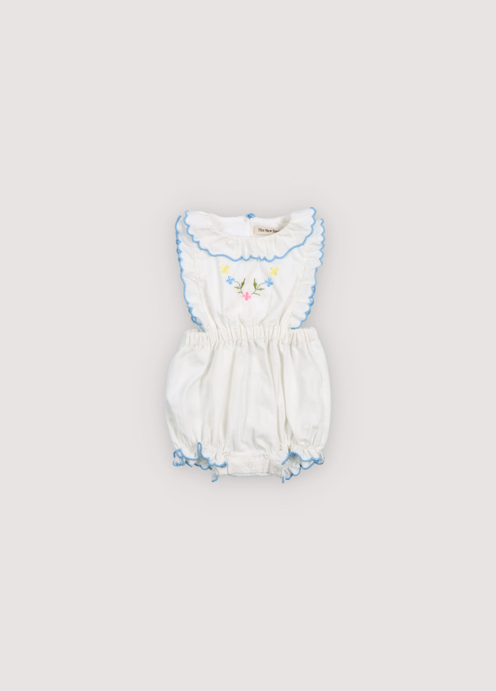 Hermione Baby Romper in 100% white cotton baize fabric with flower embroidery. Romper with gathered neckline and powder blue embroidery, ruffles with embroidery, and elastic waistband. Spring Summer Collection. The New Society.