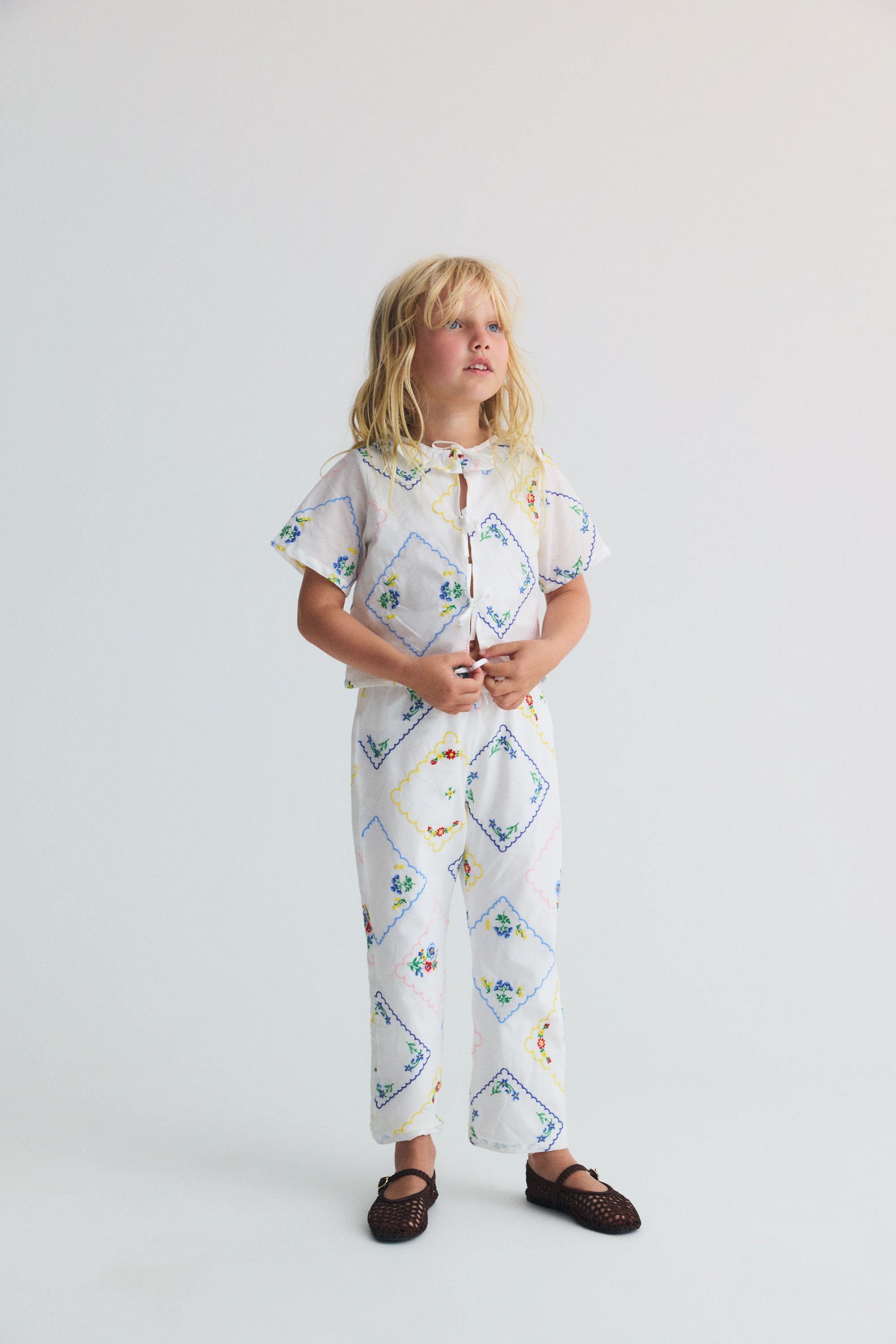 Délicate et charmante, cette blouse pour bébé 100 % coton, fabriquée au Portugal, présente de superbes broderies florales multicolores partout.