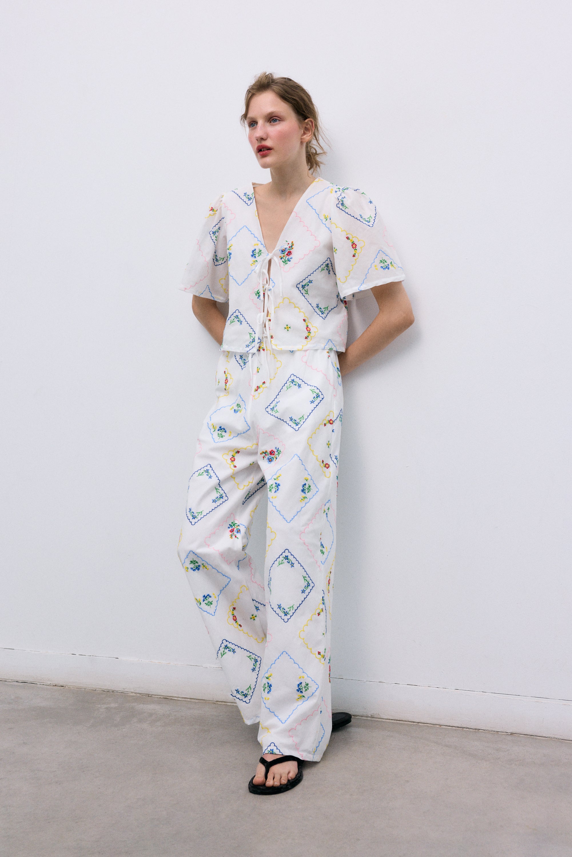 Délicate et charmante, cette blouse 100 % coton, fabriquée au Portugal, présente d'exquises broderies florales multicolores partout.