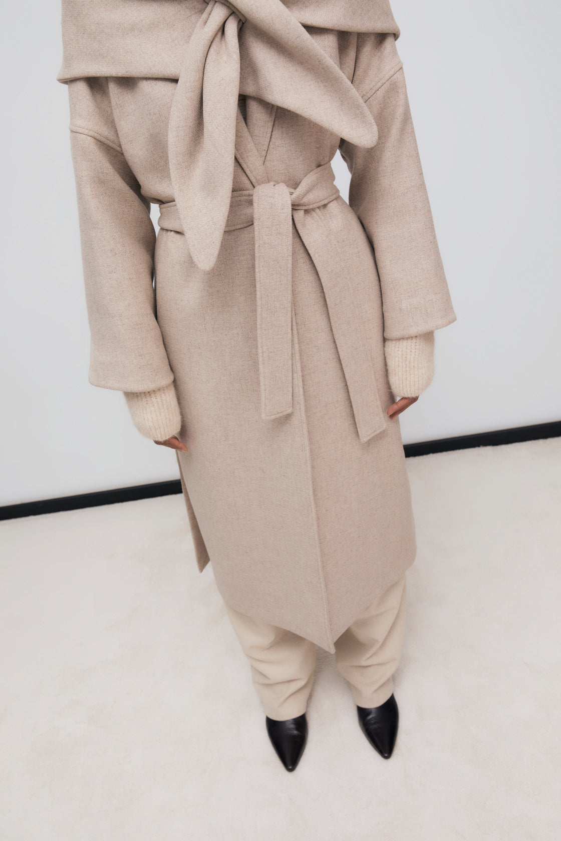 Long wool coat with lapels and side slits. It is double-breasted with a matching fabric belt. It comes with a scarf made from the same fabric.