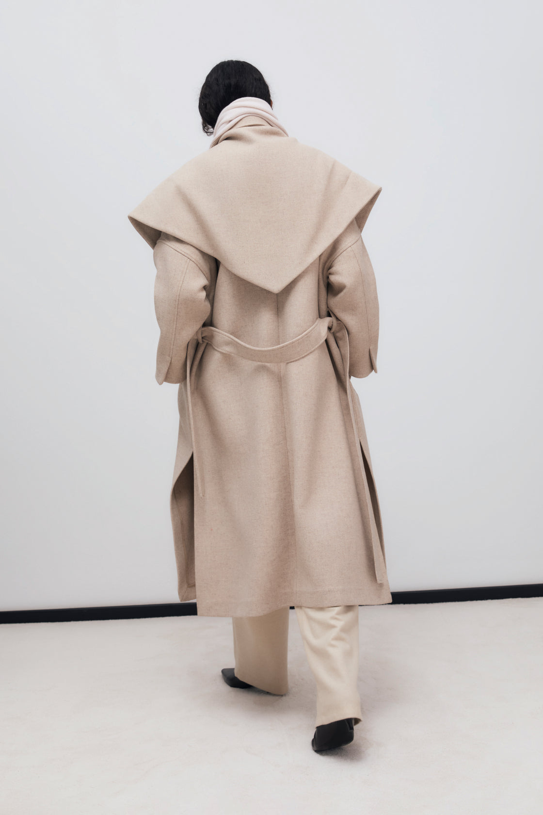 Long wool coat with lapels and side slits. It is double-breasted with a matching fabric belt. It comes with a scarf made from the same fabric.