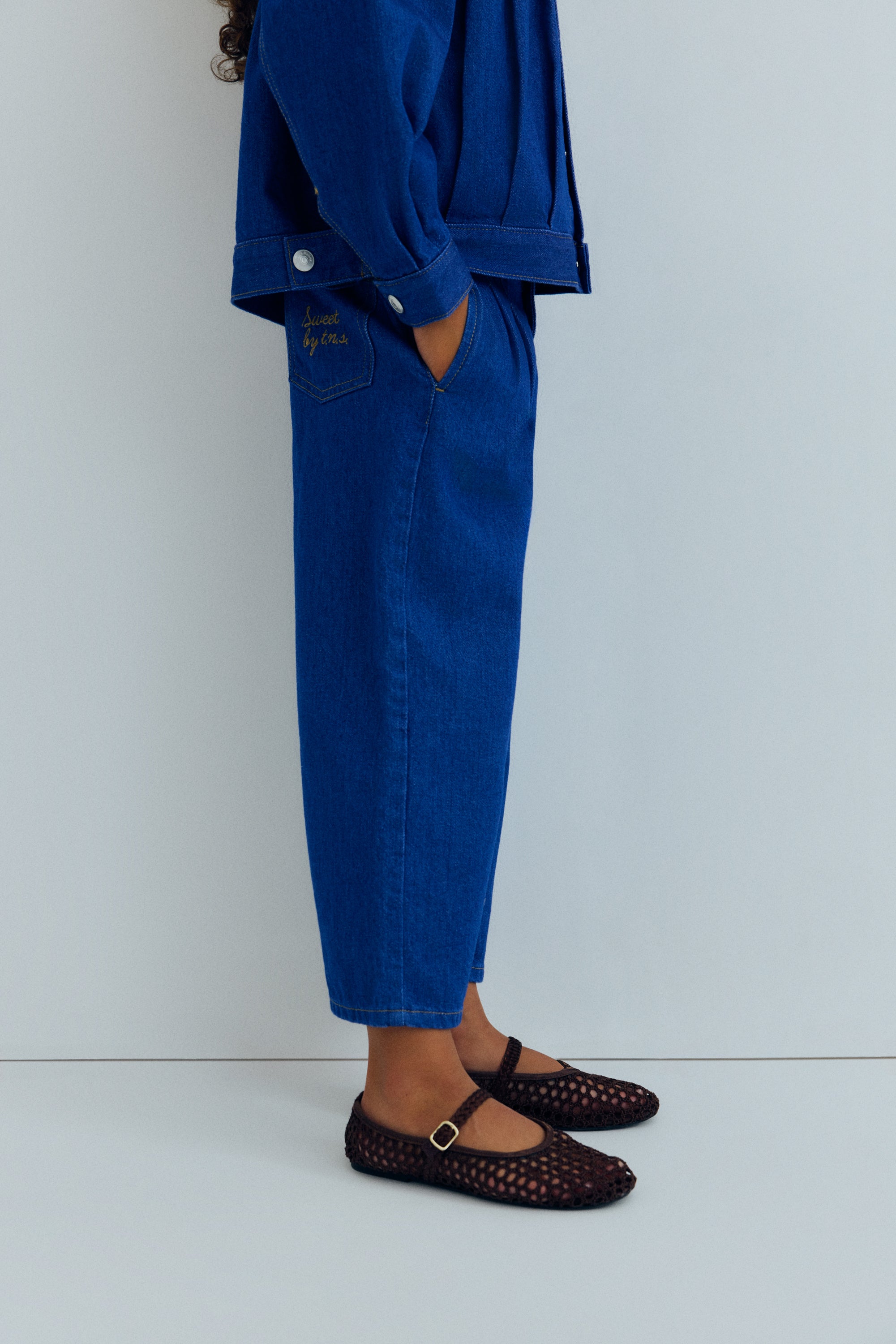Wide leg denim trousers with front pleats that enhance the relaxed silhouette.
