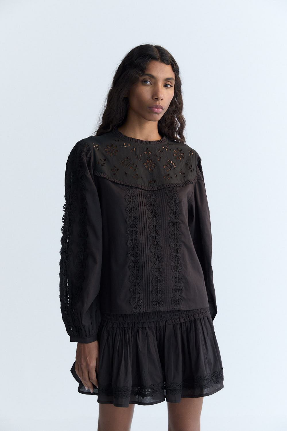 Delicate and elegant, this cambric blouse in Eclipse Noir features an embroidered yoke, soft ruffles, and intricate lace detailing on the body and sleeves. A back keyhole opening with a tone-on-tone button adds a subtle, refined finishing touch, enhancing the blouse’s timeless and sophisticated look.