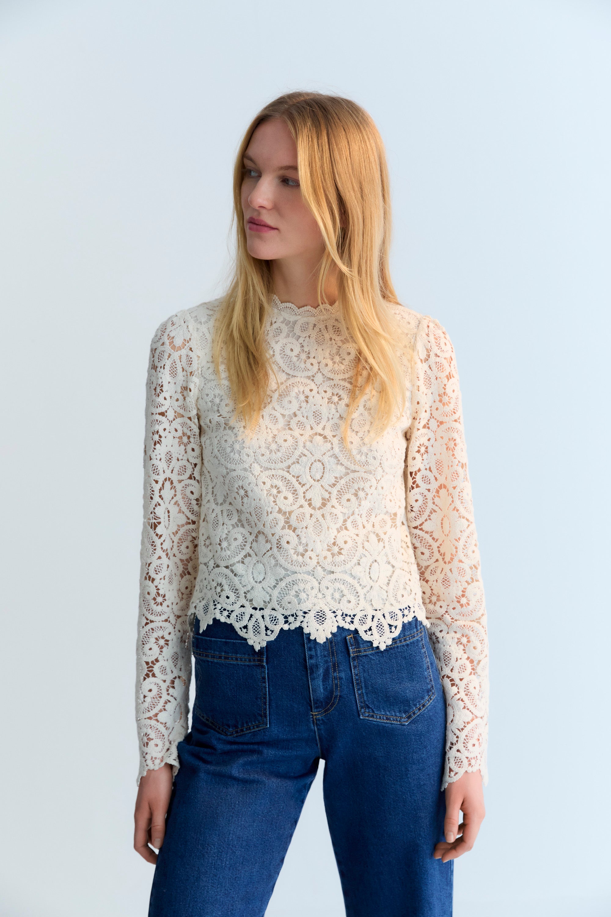 The Lara blouse is a very special crochet piece in off-white, featuring fitted sleeves with subtle volume at the shoulders and a back opening with a button closure.