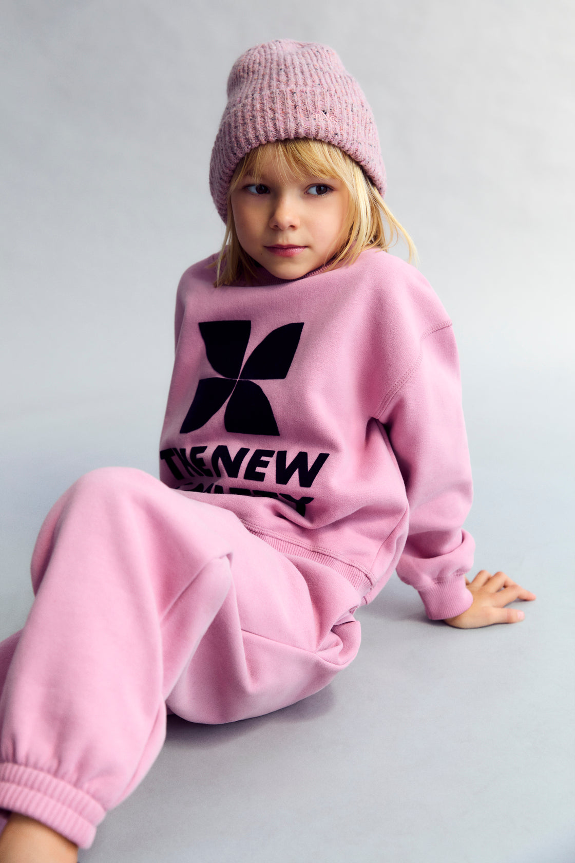 Child wearing a pink outfit with a black logo on a light gray background