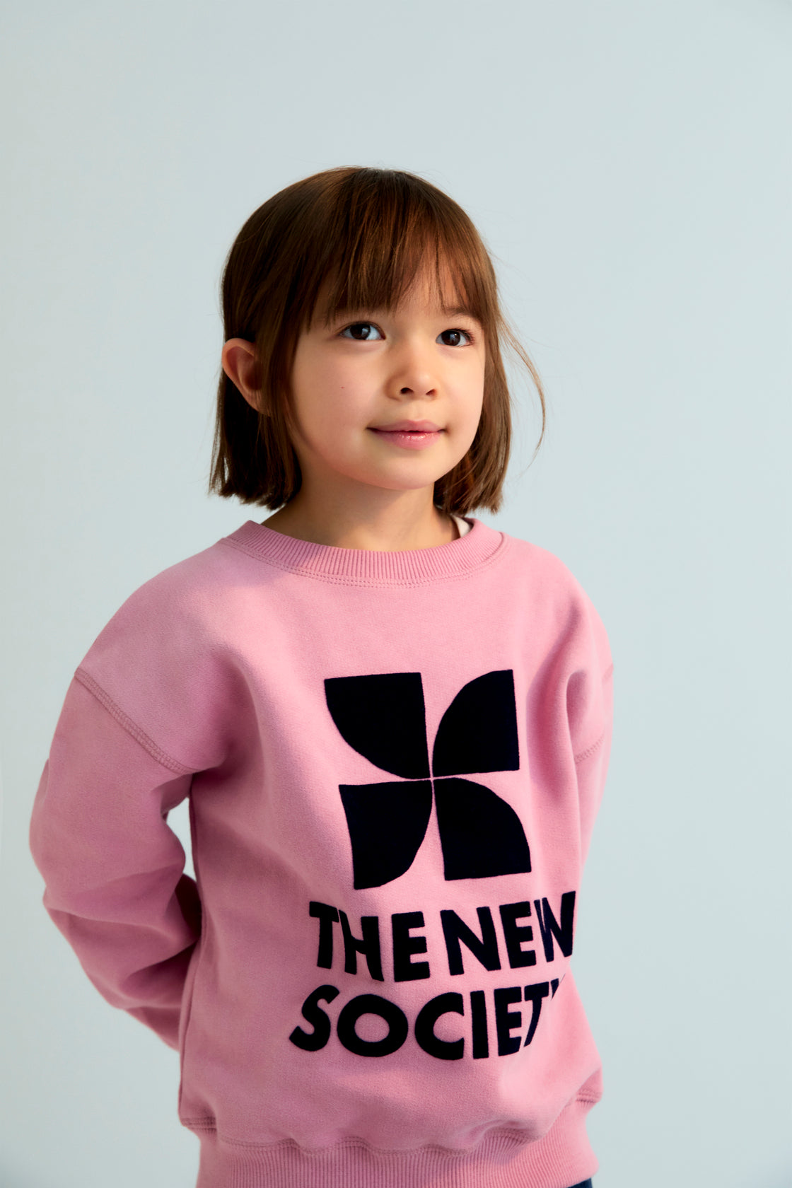 Child wearing a pink sweatshirt with a black logo and text on a light gray background