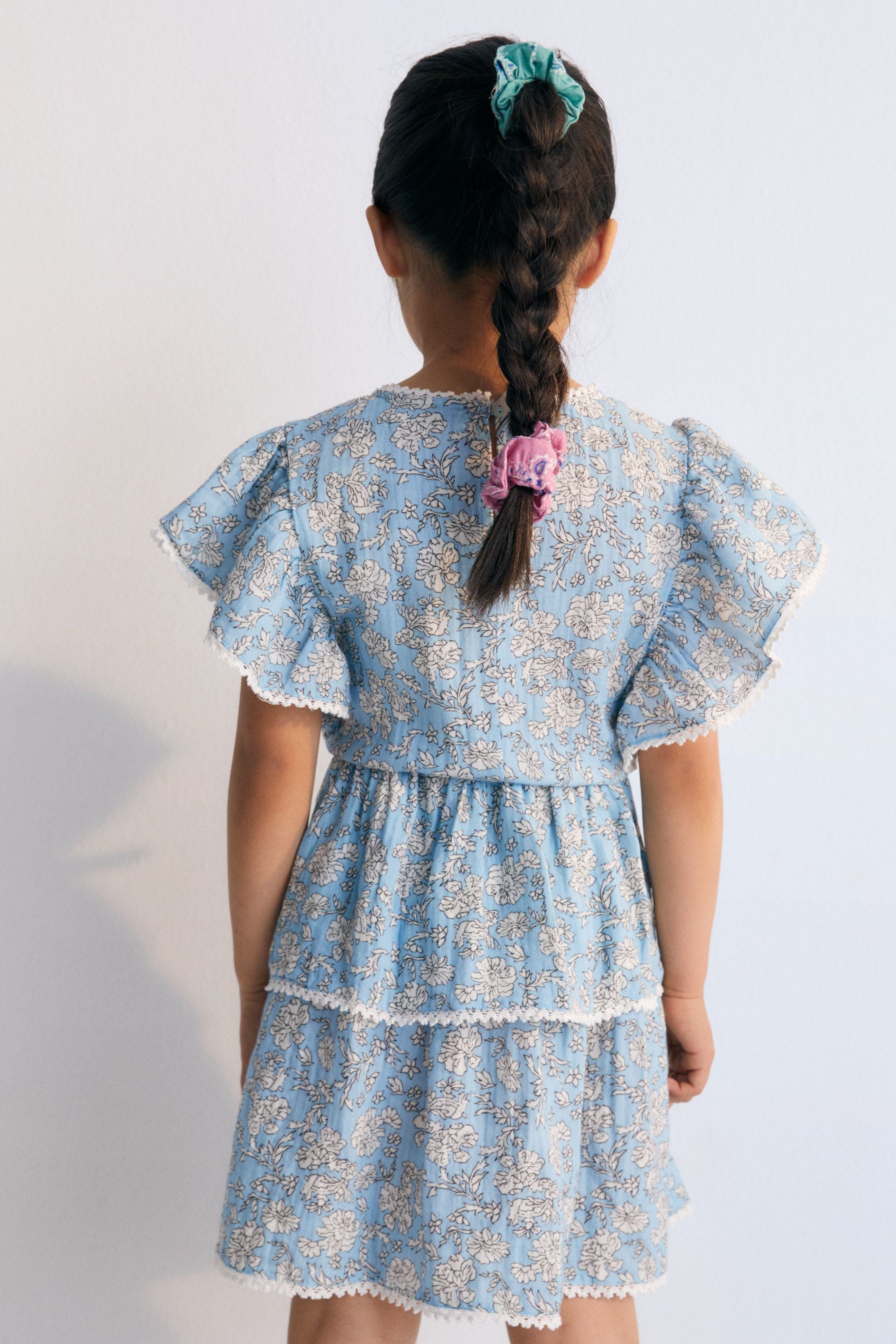 Melina Dress in 100% cotton muslin with our peony powder blue print. The blouse features a ruffle from the shoulder to the hem, a high neckline, and lace detail on the neckline and ruffle. The New Society.