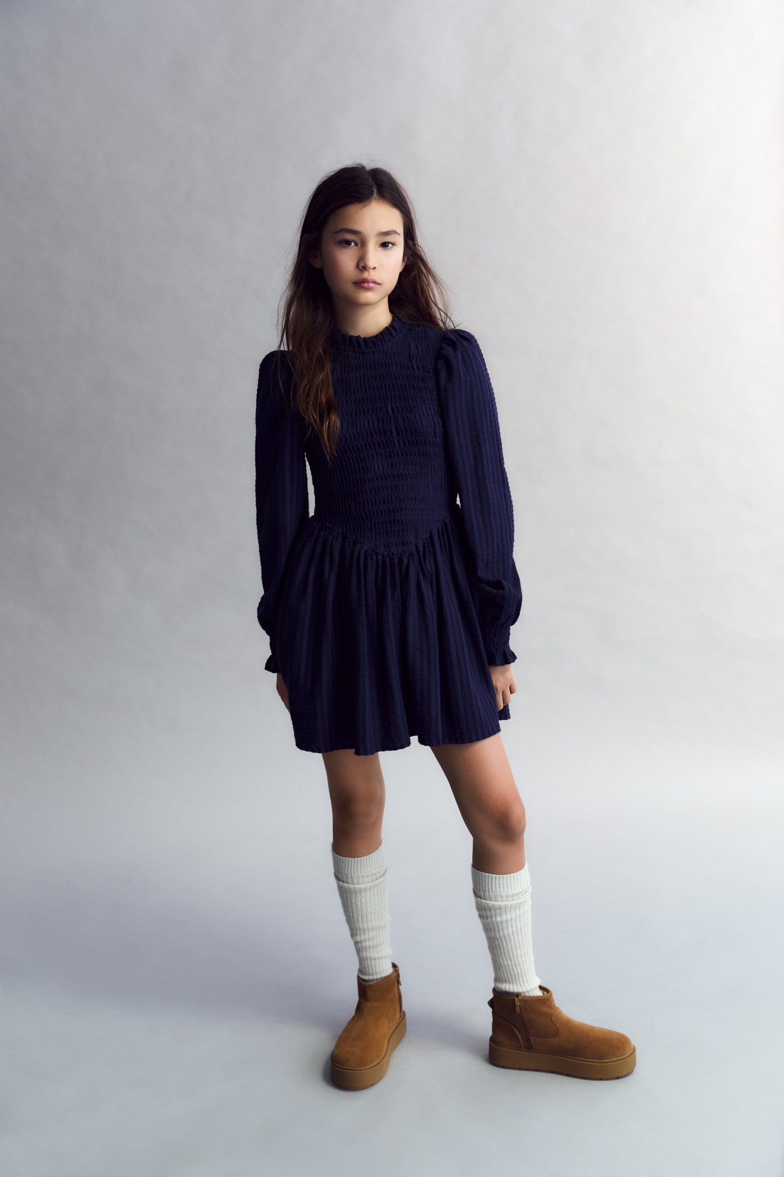 Short seersucker dress with a smocked bodice and V-shaped finish. It features puffed sleeves and a round neckline with a ruffle detail.