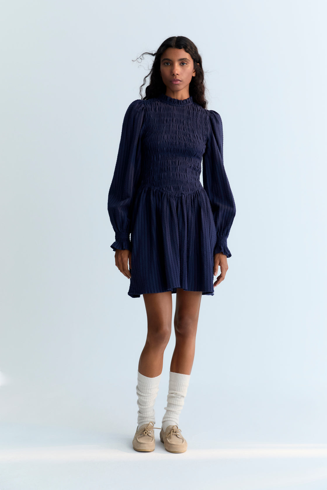 Short seersucker dress with a smocked bodice and V-shaped finish. It features puffed sleeves and a round neckline with a ruffle detail.