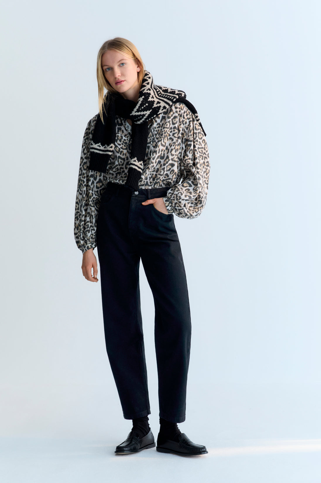 Person wearing a patterned coat, black scarf, and black pants on a white background