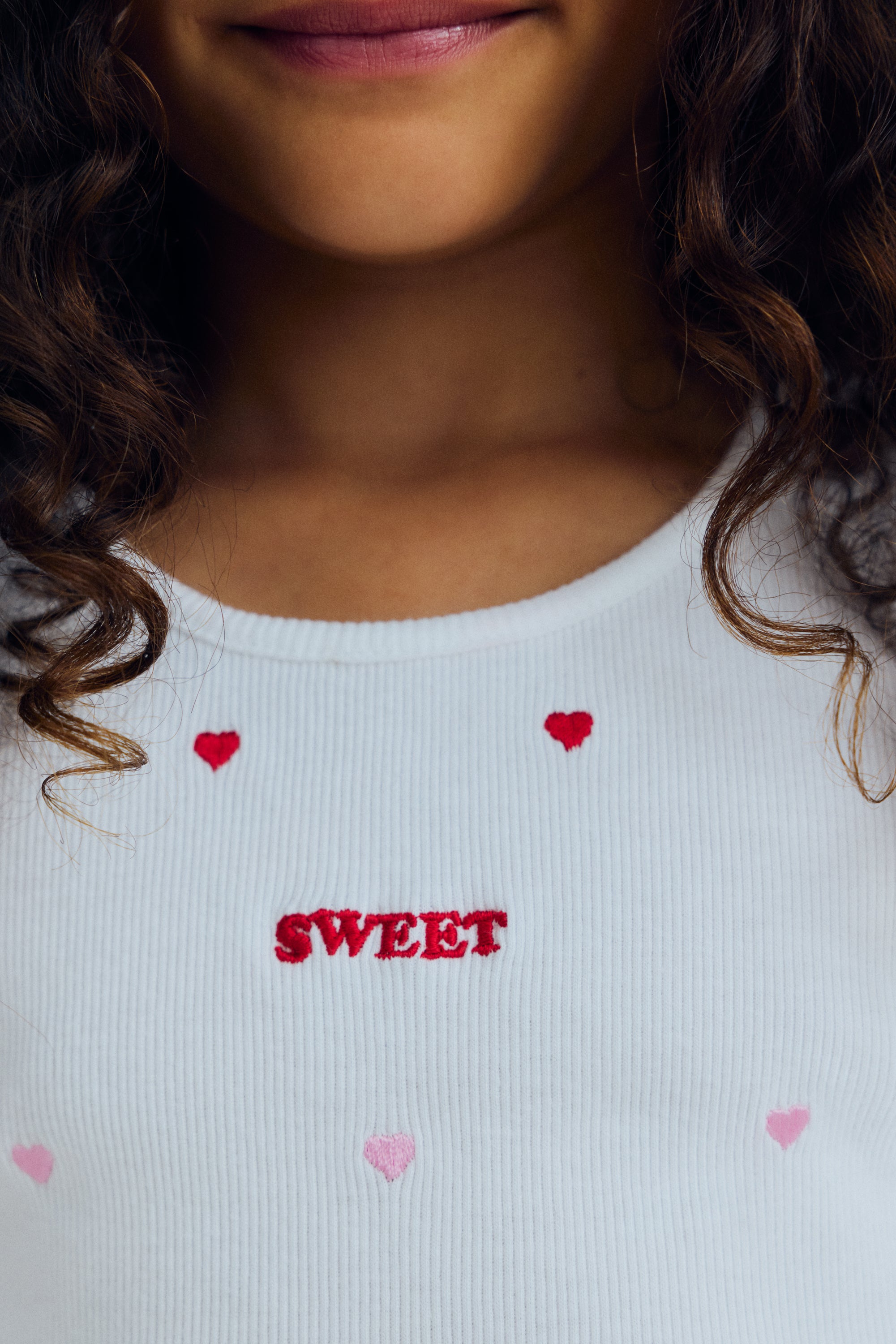 A playful cotton tank top featuring red heart patterns on a soft beige background. Crafted in lightweight, breathable cotton for everyday comfort, it offers a relaxed fit and a timeless, cheerful look.