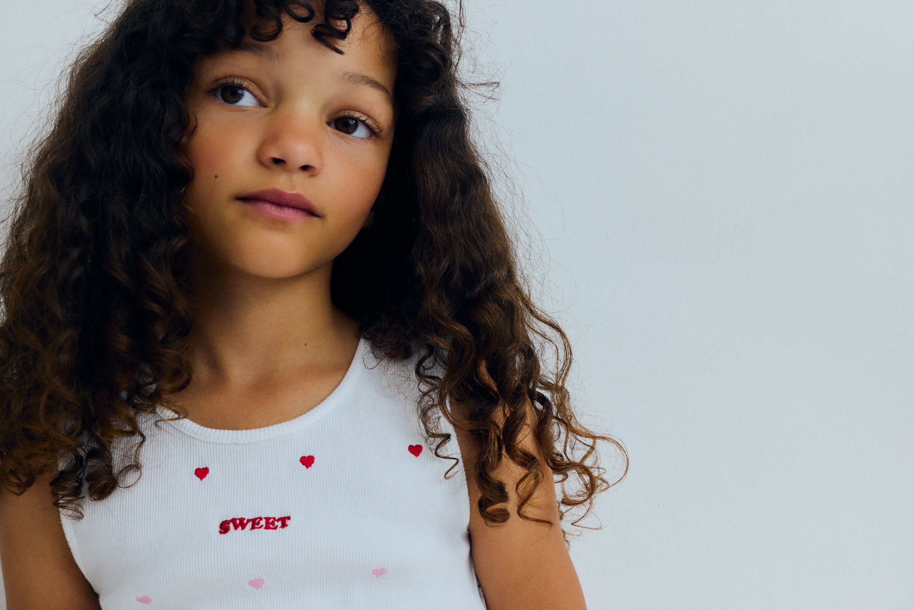 A playful cotton tank top featuring red heart patterns on a soft beige background. Crafted in lightweight, breathable cotton for everyday comfort, it offers a relaxed fit and a timeless, cheerful look.