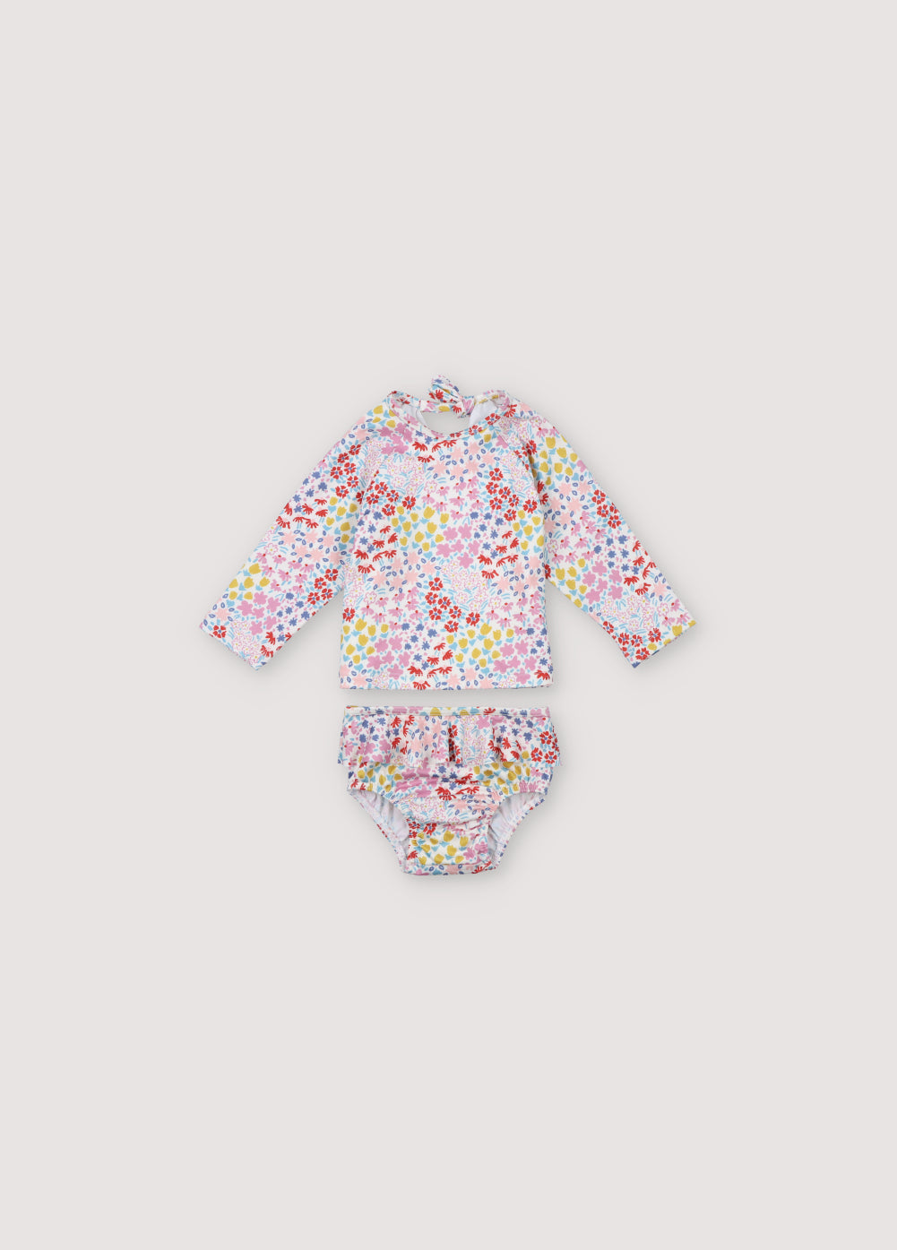 Two-piece swimsuit for baby girls featuring a lovely floral print. It includes a long-sleeved swim shirt with an opening at the back with a bow, and a bottom part with ruffle detailing on the sides. Sprin Summer Collection. The New Society.