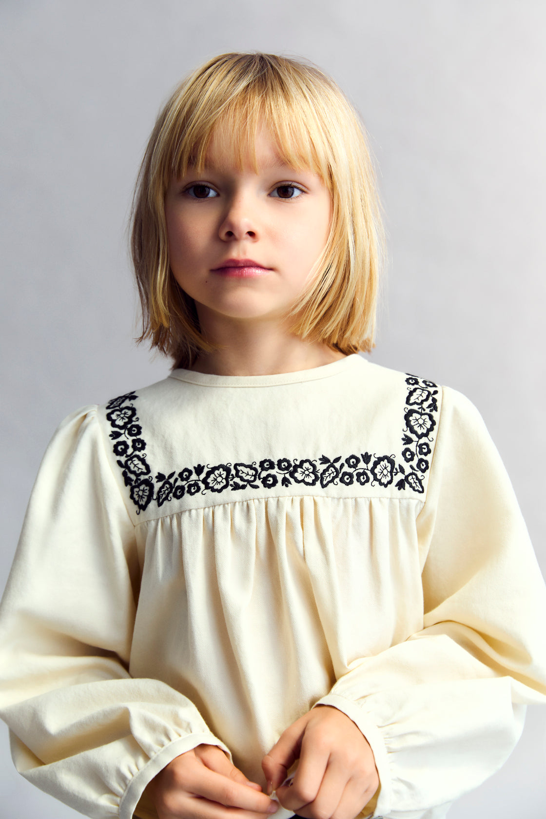 Blouse with a bust cut and gathering detail, featuring delicate contrast embroidery. It has a back opening with a tear and button closure.