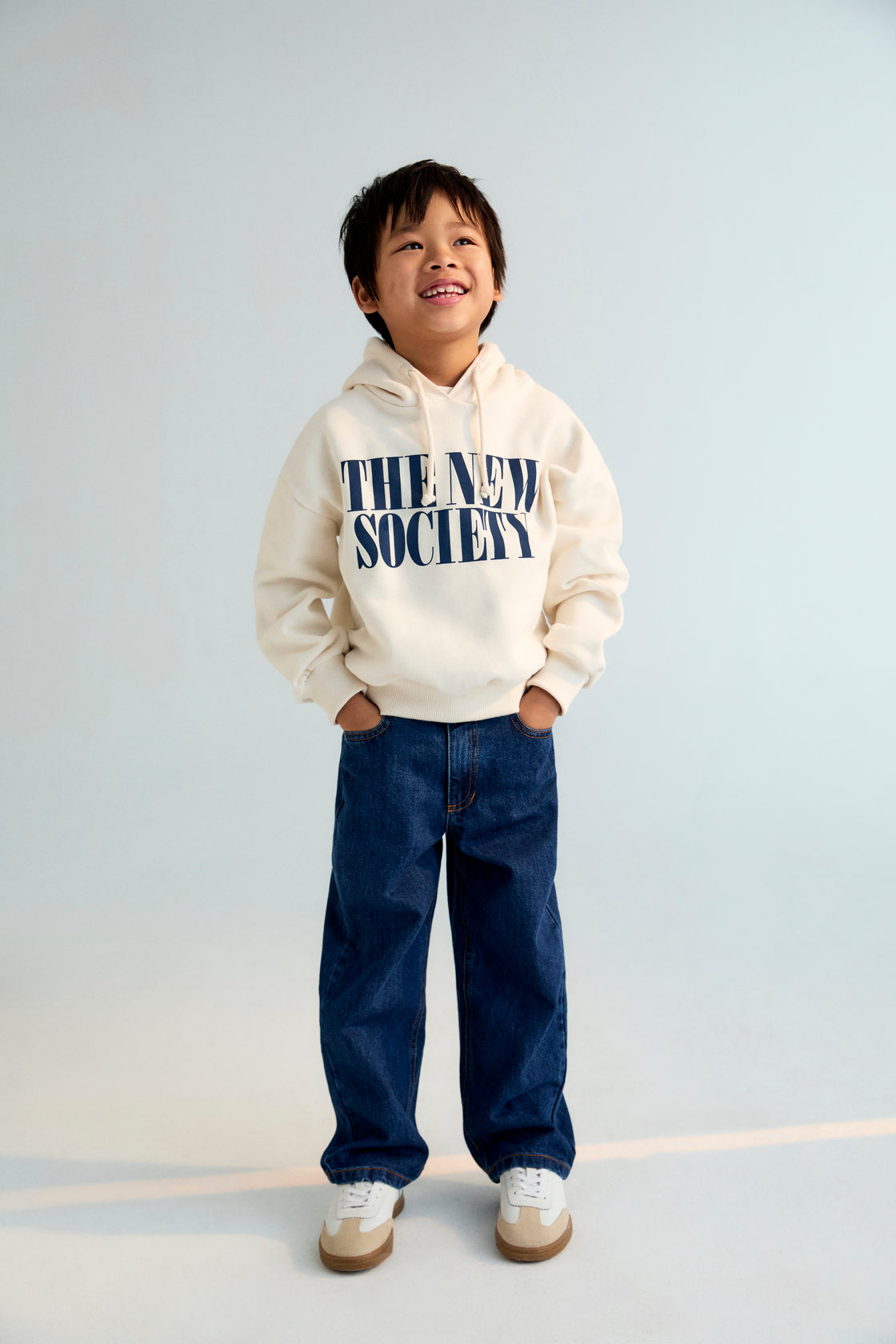 Child wearing a 'The New Society' hoodie on a plain background