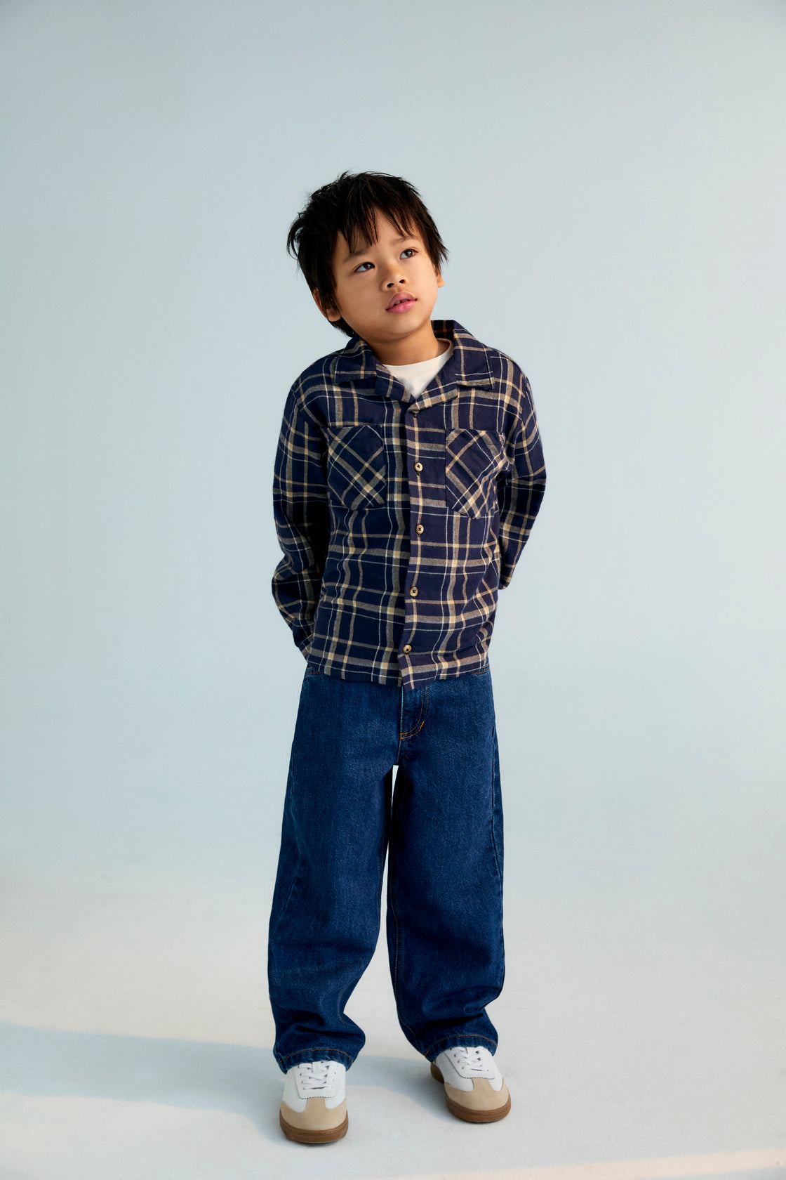 Child wearing a plaid shirt and blue jeans on a plain background
