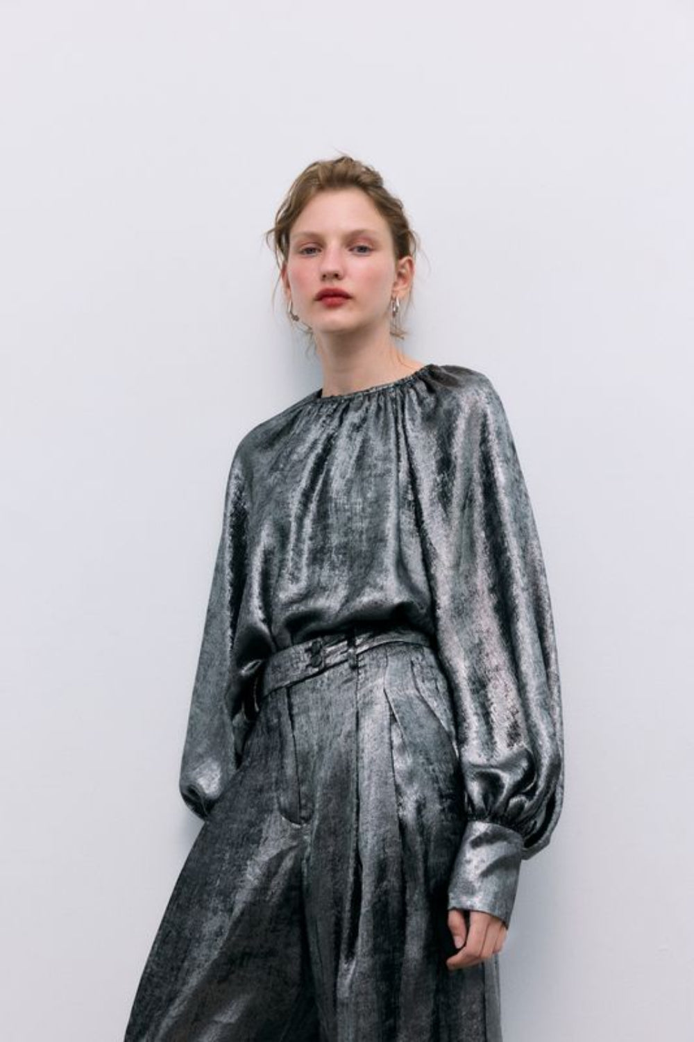 Silver shine blouse with a round neckline and gathered detailing, puffed sleeves with wide cuffs, and covered buttons in the same fabric. It features a back opening with a keyhole and button closure.