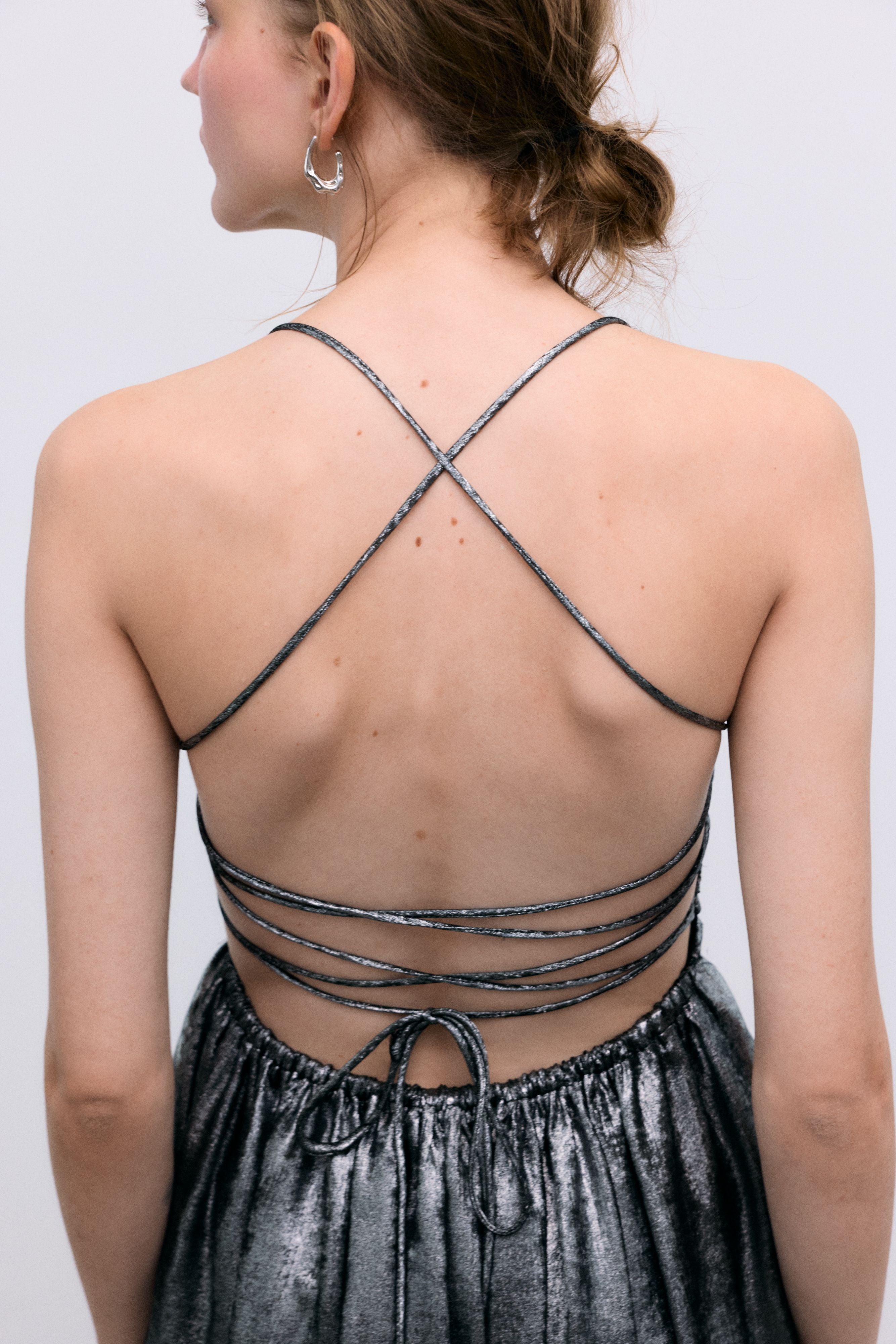 Silver shine dress with a waist cut and front ruching. It features spaghetti straps that cross at the back and a zipper closure.