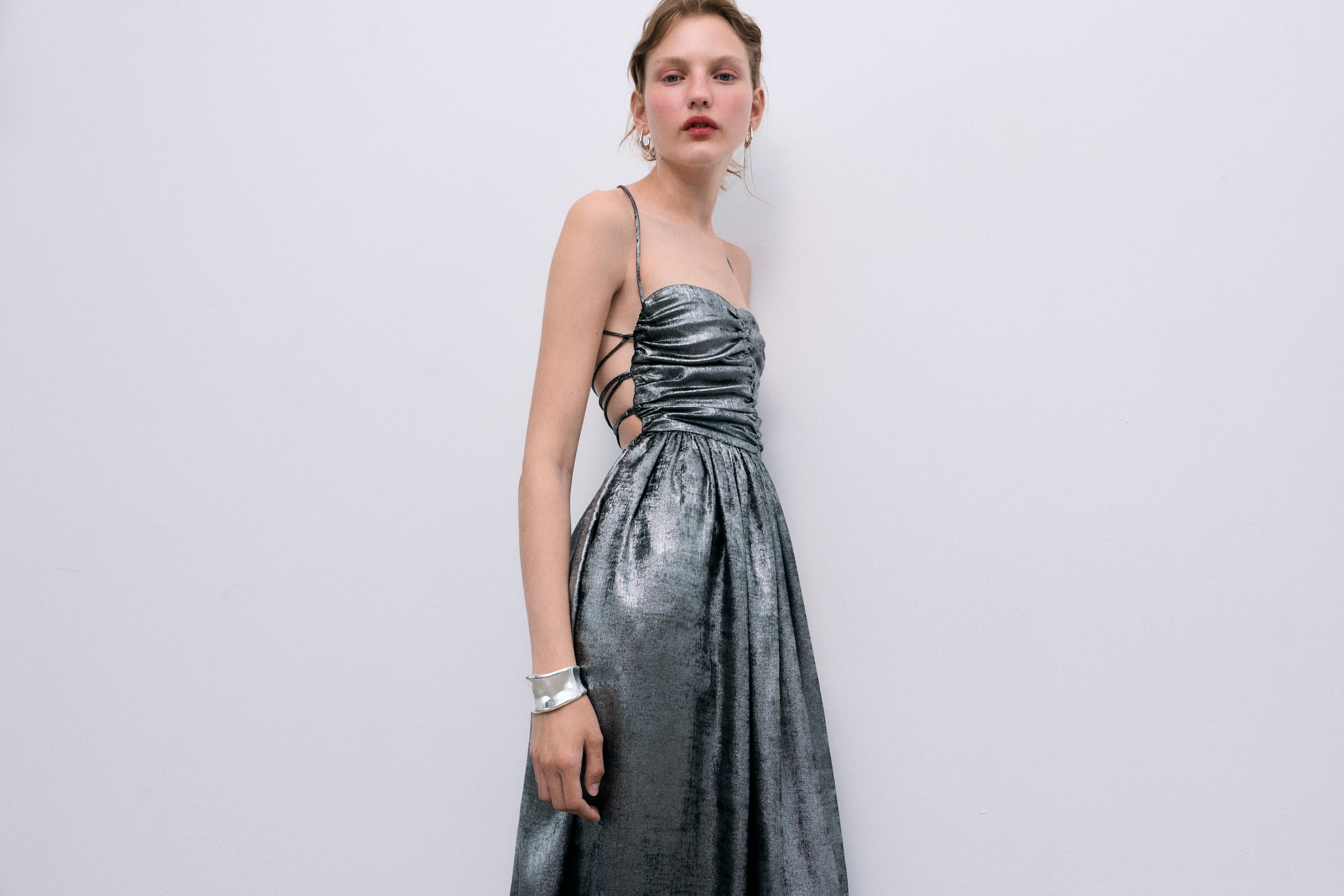 Silver shine dress with a waist cut and front ruching. It features spaghetti straps that cross at the back and a zipper closure.