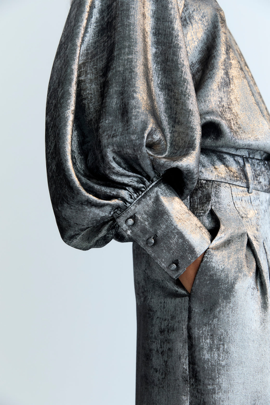 Silver shine blouse with a round neckline and gathered detailing, puffed sleeves with wide cuffs, and covered buttons in the same fabric. It features a back opening with a keyhole and button closure.