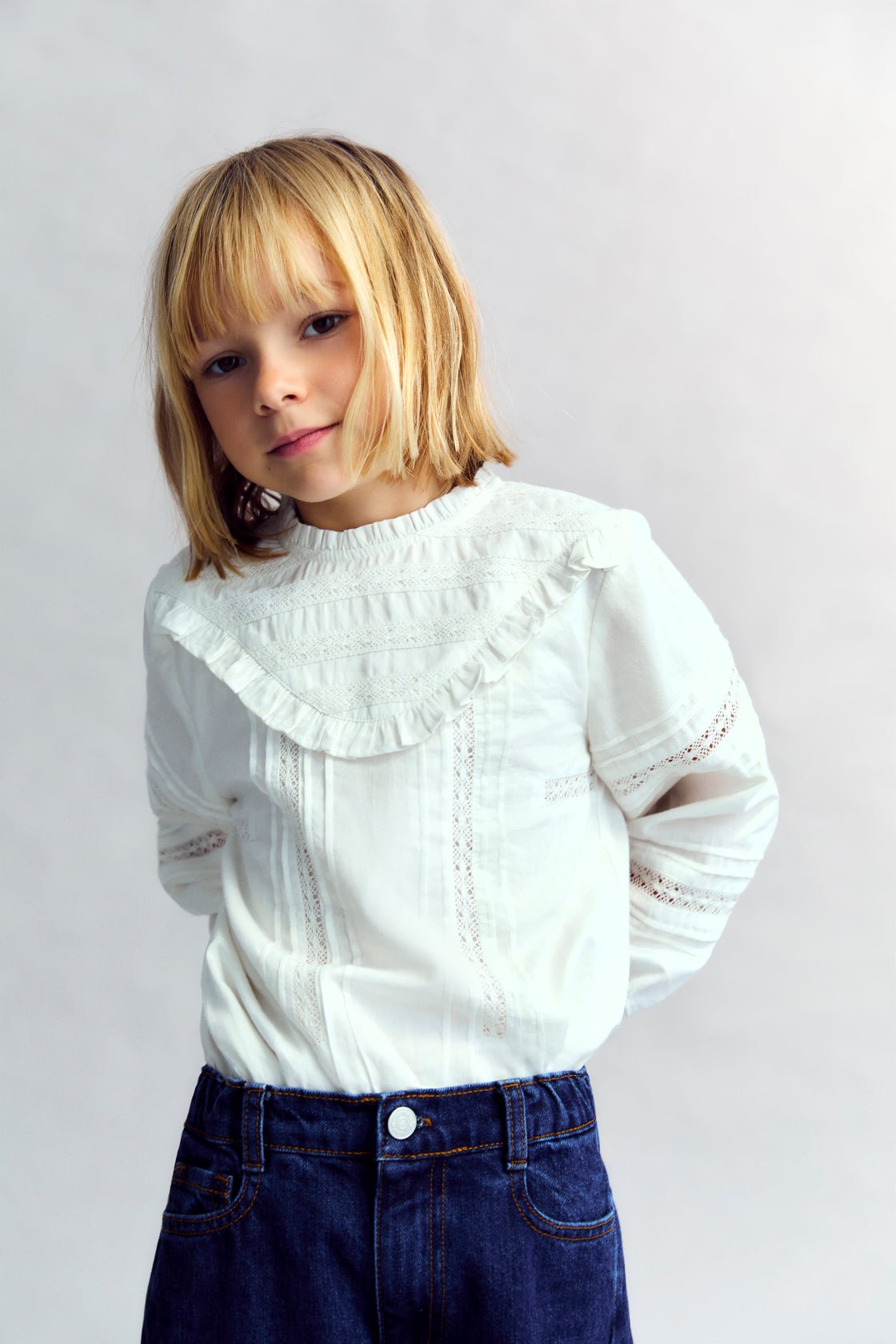 Romantic-style blouse with a front yoke detail in lace and a ruffle finish, along with lace details on the sleeves. It features a round neckline with a small ruffle trim and a back opening with a button closure.