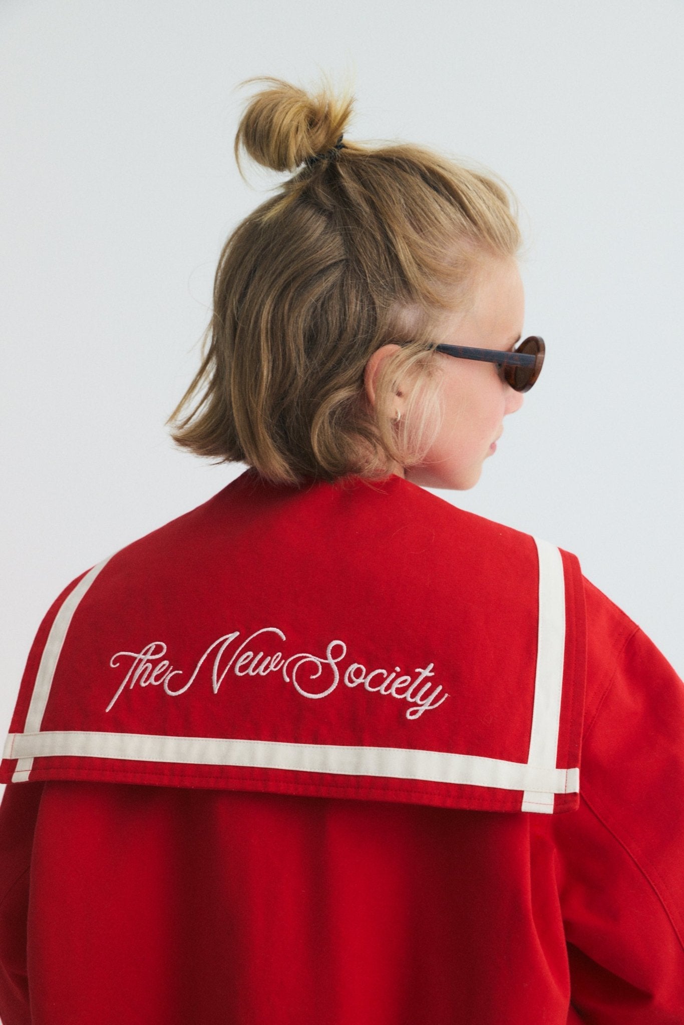 Chaqueta estilo bomber en un rojo vibrante, con un exclusivo cuello marinero, logotipo de la Sociedad bordado en la espalda y rayas en contraste.