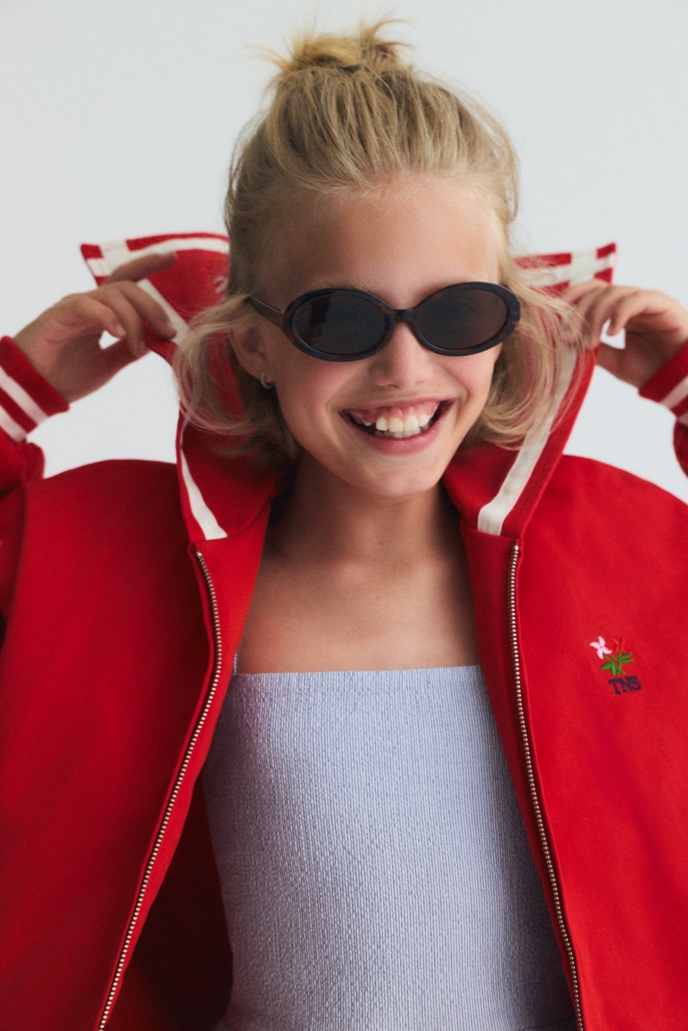 Chaqueta estilo bomber en un rojo vibrante, con un exclusivo cuello marinero, logotipo de la Sociedad bordado en la espalda y rayas en contraste.