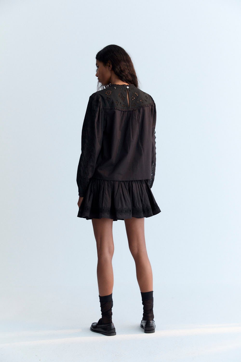 Delicate and elegant, this cambric blouse in Eclipse Noir features an embroidered yoke, soft ruffles, and intricate lace detailing on the body and sleeves. A back keyhole opening with a tone-on-tone button adds a subtle, refined finishing touch, enhancing the blouse’s timeless and sophisticated look.