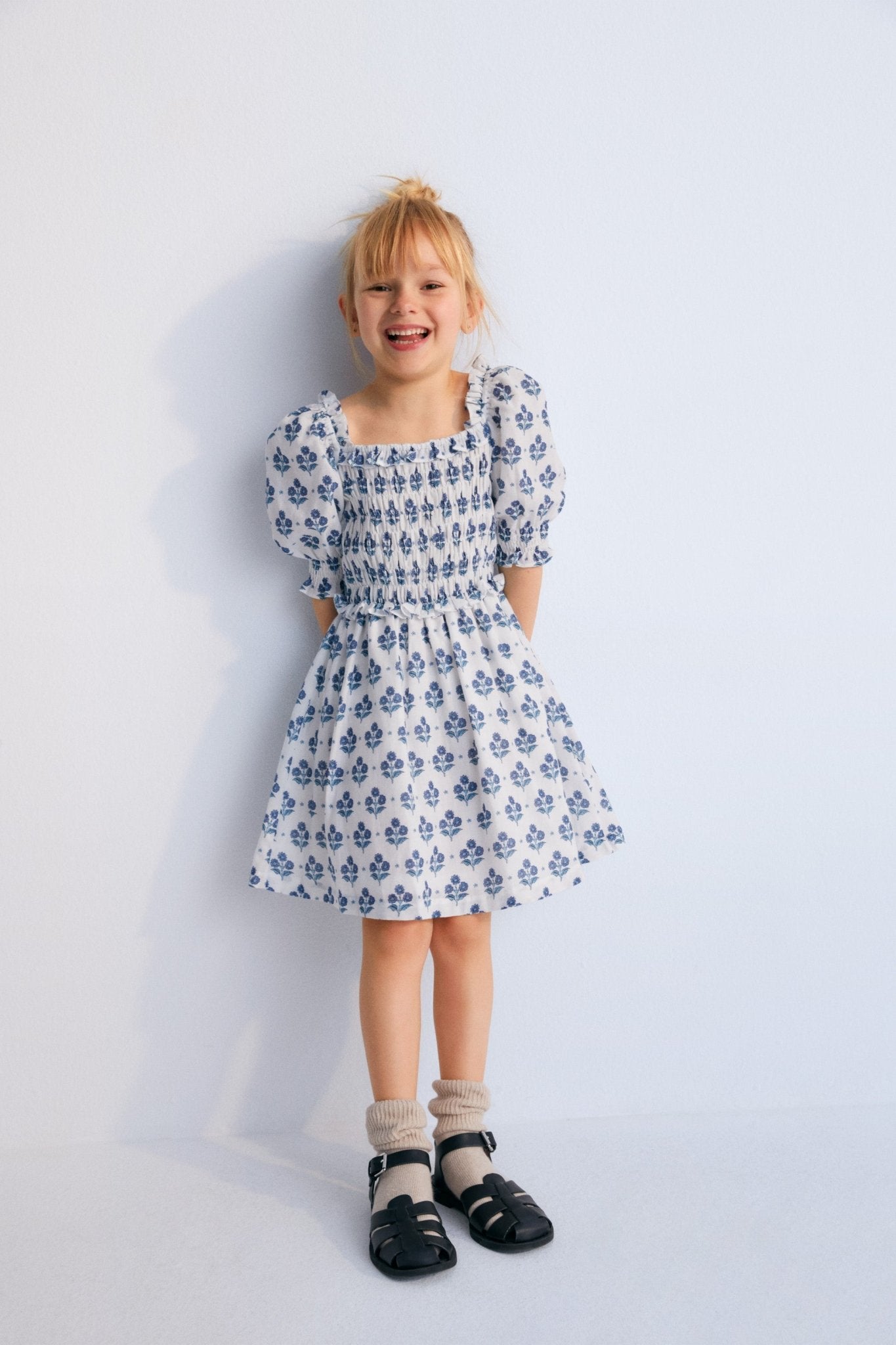 Eleni Dress in 100% cotton muslin fabric with our hyacinth print. The dress features a square neckline with smocking all over, puffed sleeves with smocking and a final ruffle, and a skirt with lots of volume.