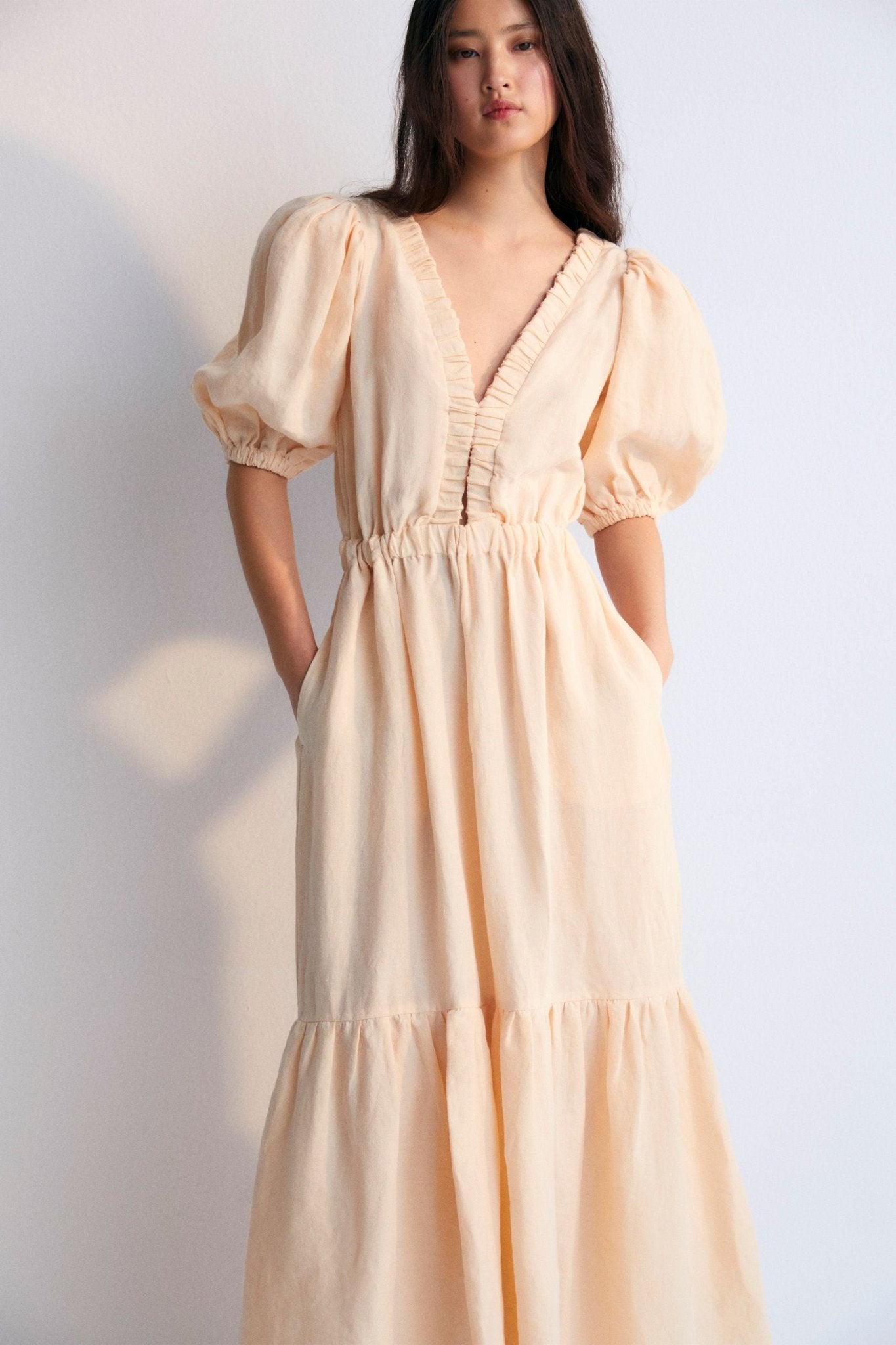 Hera Woman Dress 3 in 100% linen, available in two colors: caviar and macadamia. V-neck with elastic band, puffed sleeves, and an elastic waistband to generate volume in the skirt. Spring Summer Collection. The New Society.