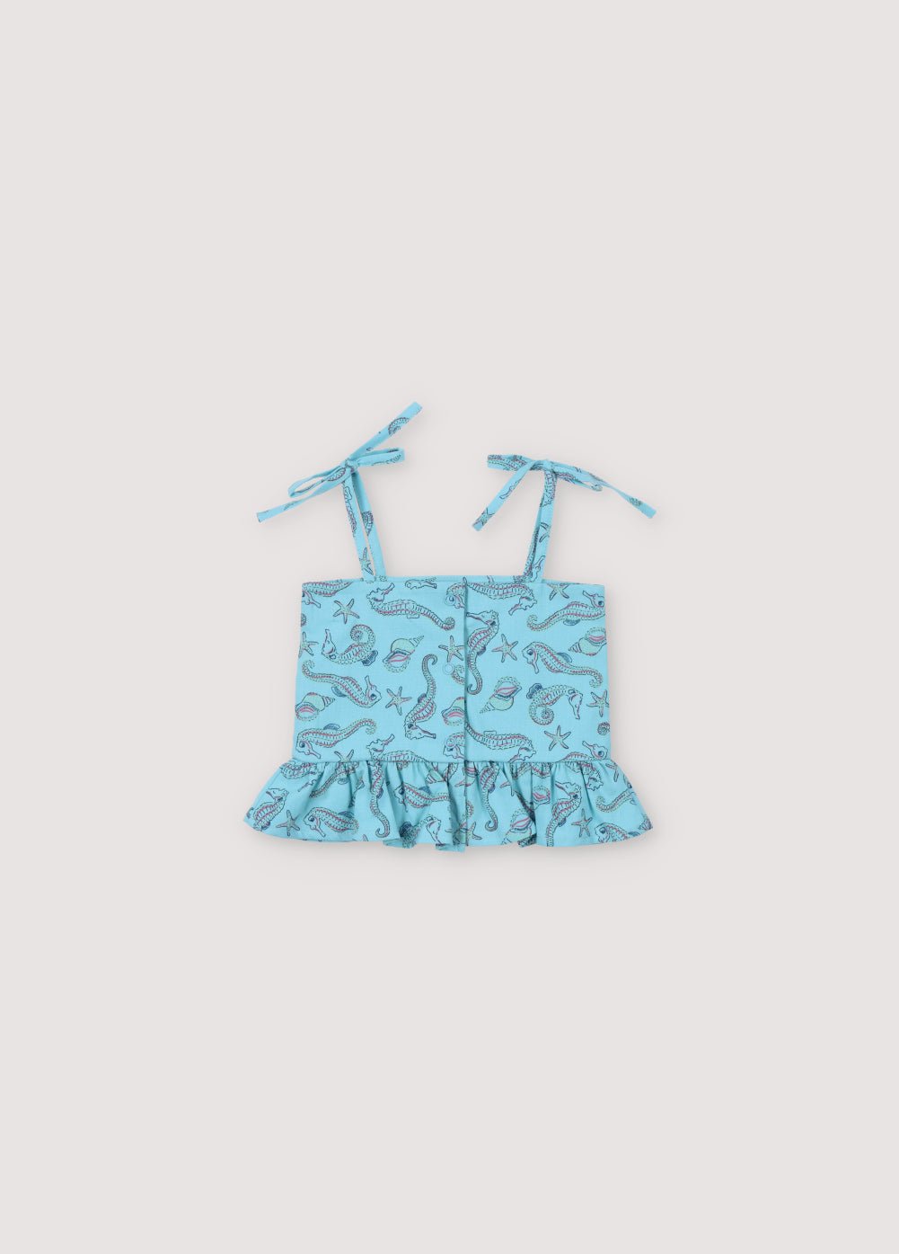 Haut bébé Io en tissu 100% coton avec notre imprimé hippocampes, caractérisé par un détail volant sur le bas, des boutons en nacre au dos et des bretelles. Collection printemps-été. The New Society.