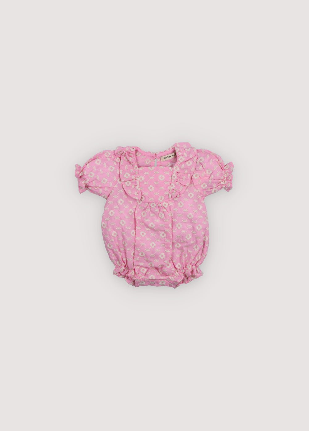 Barboteuse bébé Isidora en voile d'hibiscus avec broderie cot-pes en macadamia. Encolure carrée, volants latéraux, manches courtes bouffantes et élastique avec détail volants au niveau des jambes. Collection Printemps Été. The New Society.