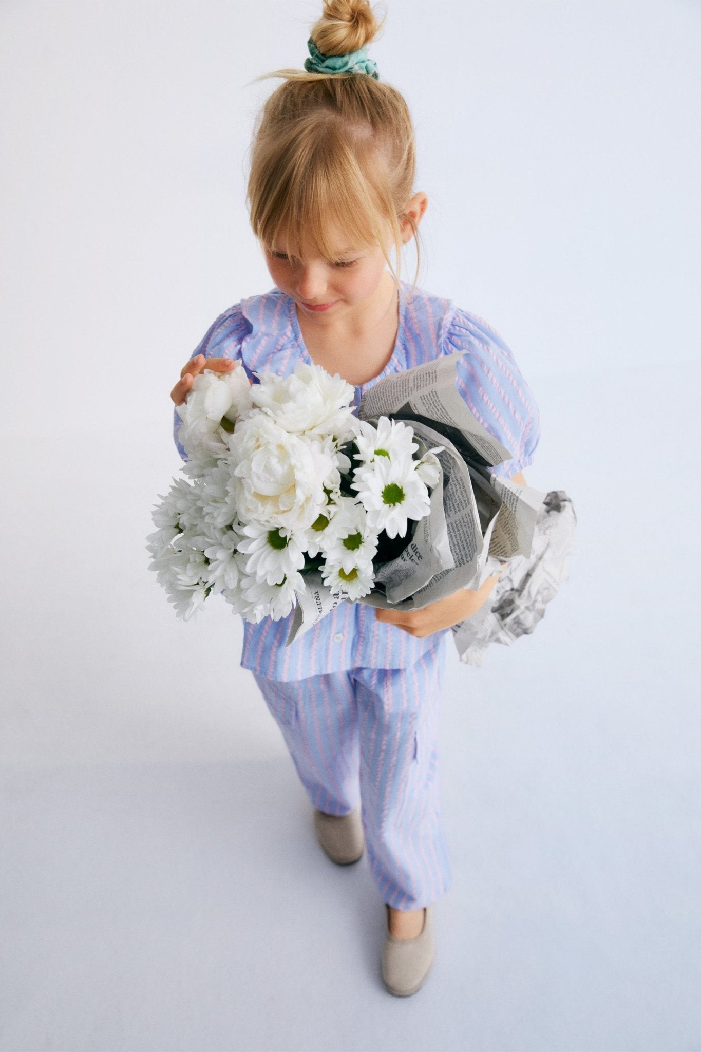 Kythira Blouse in 100% cotton striped fabric with cut details and ruffles at the hem, ruffled neckline, puffed short sleeves, and mother-of-pearl flower-shaped buttons.