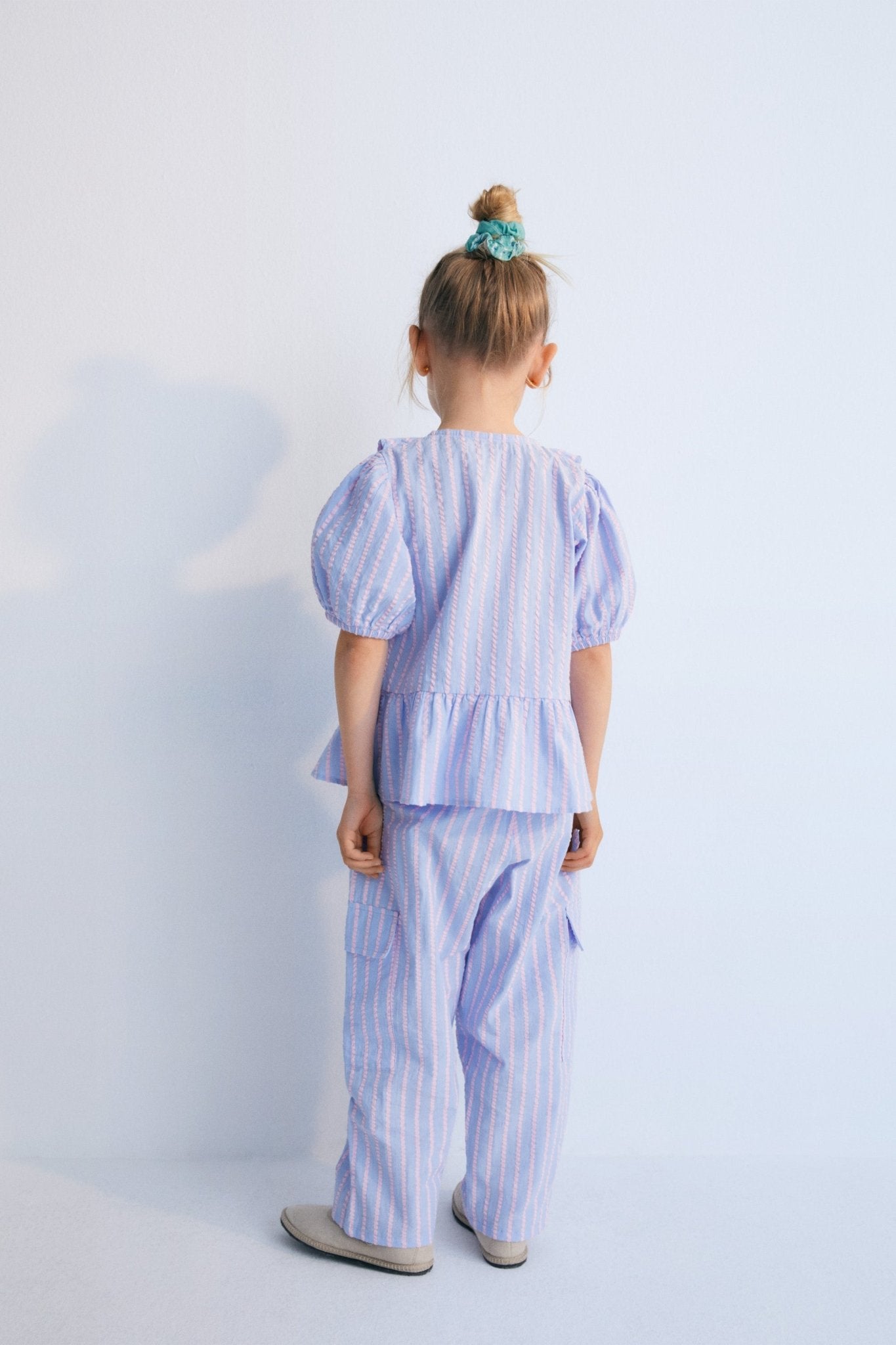 Kythira Blouse in 100% cotton striped fabric with cut details and ruffles at the hem, ruffled neckline, puffed short sleeves, and mother-of-pearl flower-shaped buttons.