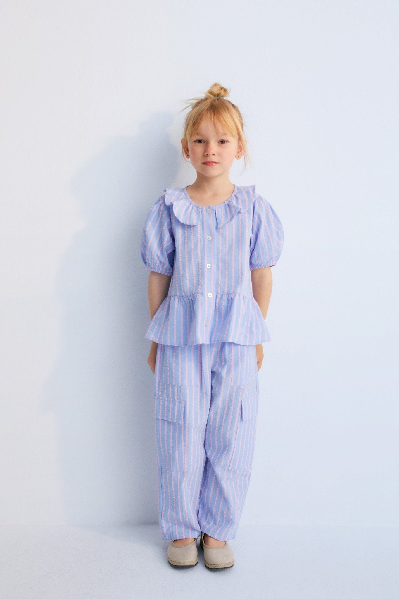 Kythira Blouse in 100% cotton striped fabric with cut details and ruffles at the hem, ruffled neckline, puffed short sleeves, and mother-of-pearl flower-shaped buttons.