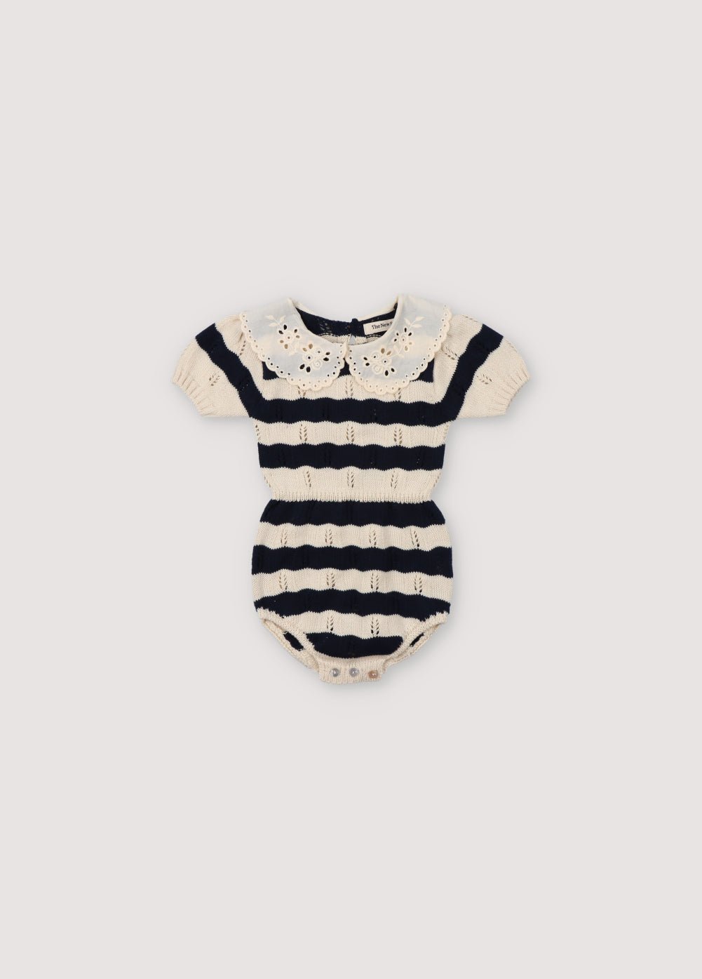 Barboteuse à rayures bicolores avec col en dentelle contrastée. Il a une taille et des poignets élastiques, une ouverture avec des boutons-pression et un dos avec une patte et des boutons en nacre. Collection Printemps Été. The New Society.