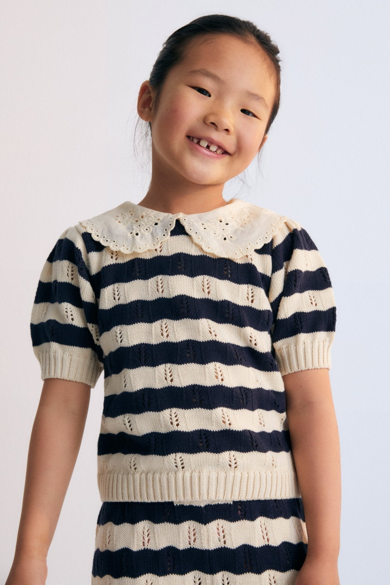 Bicolor striped short-sleeved knit sweater with delicate contrast lace collar detail. It features elastic ribbing at the hem and also elastic cuffs. It's a perfect garment to create a fun total look with the matching pants.