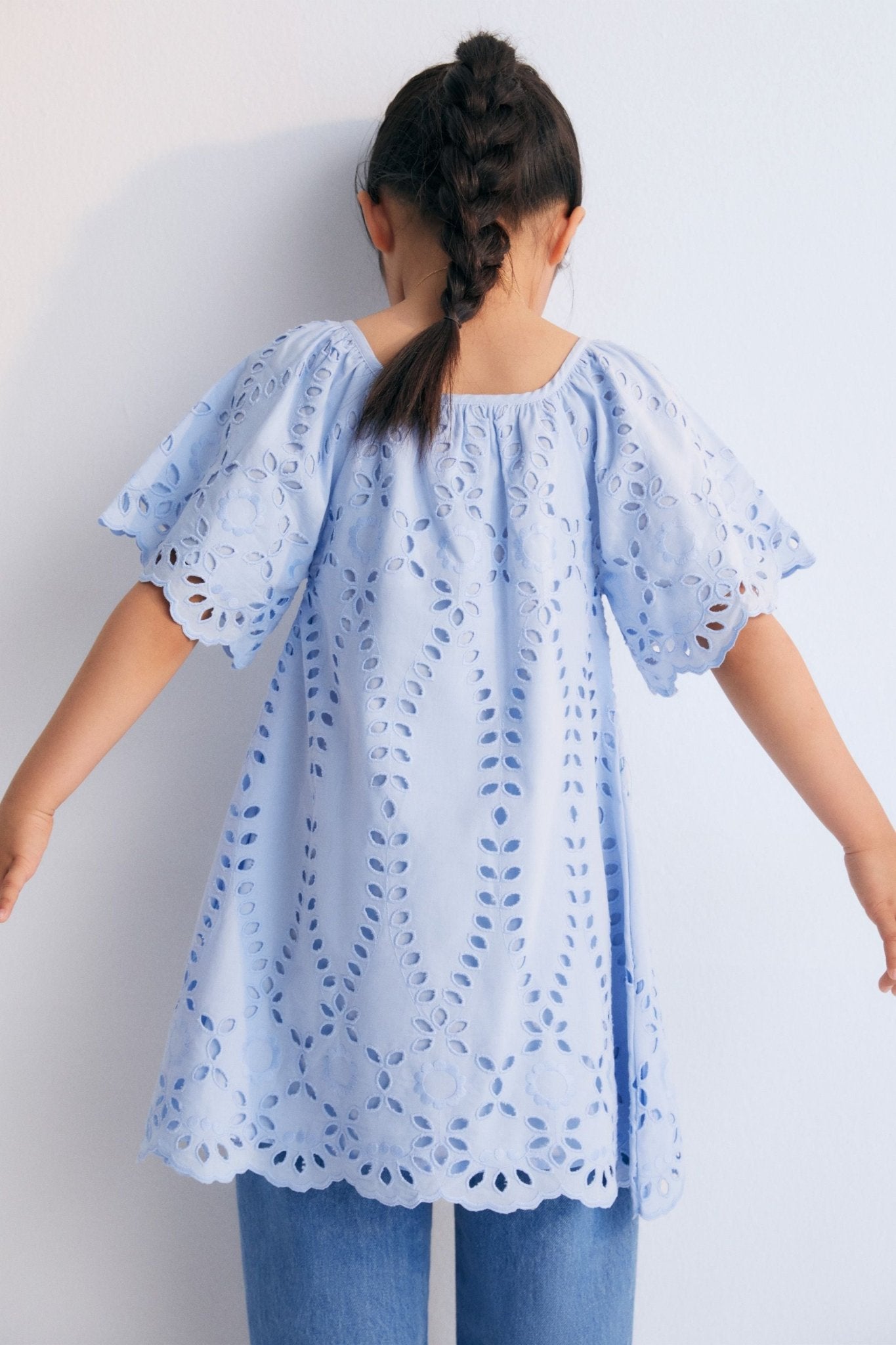 Patmos Dress in embroidered voile fabric, 100% cotton, in powder blue color. The dress features wide sleeves, gathers at the shoulders, front, and back for added volume, with embroidered fabric finishing on the sleeve cuffs and hem. Spring Summer Collection. The New Society.
