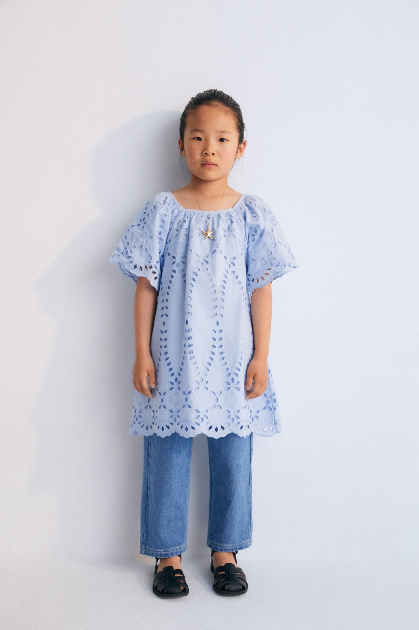 Patmos Dress in embroidered voile fabric, 100% cotton, in powder blue color. The dress features wide sleeves, gathers at the shoulders, front, and back for added volume, with embroidered fabric finishing on the sleeve cuffs and hem. Spring Summer Collection. The New Society.