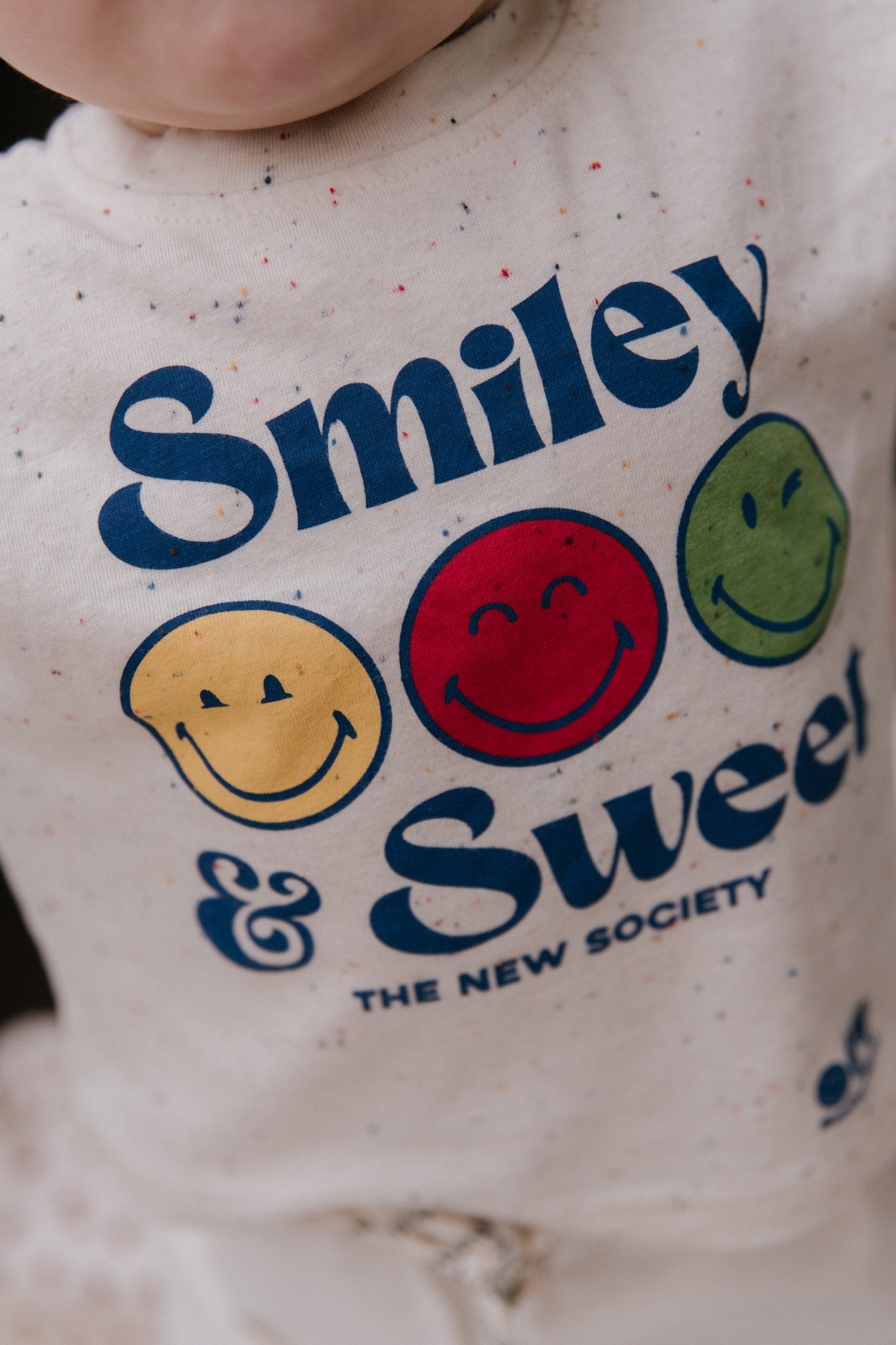 Lustiges, gesprenkeltes Jersey-T-Shirt mit SmileyWorld®-Aufdruck auf der Vorderseite und Druckknöpfen an der Schulter für einfaches Tragen, die einen verspielten, praktischen Touch verleihen.