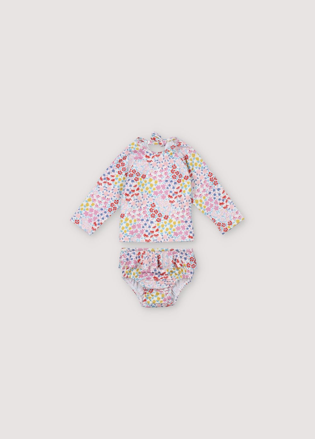 Maillot de bain deux pièces bébé fille orné d'un joli imprimé fleuri. Il comprend un maillot de bain à manches longues avec une ouverture au dos avec un nœud et un bas avec des détails volants sur les côtés. Collection Printemps Eté. The New Society.