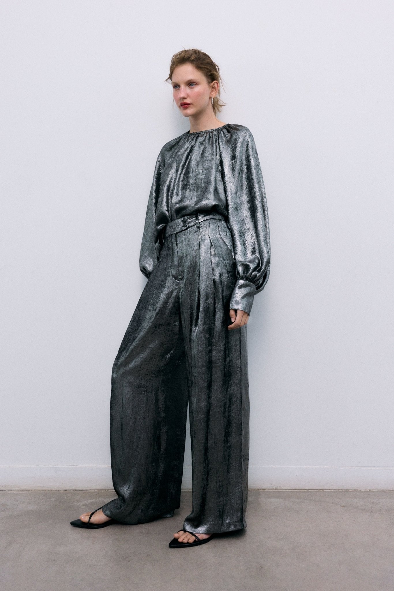 Silver shine blouse with a round neckline and gathered detailing, puffed sleeves with wide cuffs, and covered buttons in the same fabric. It features a back opening with a keyhole and button closure.