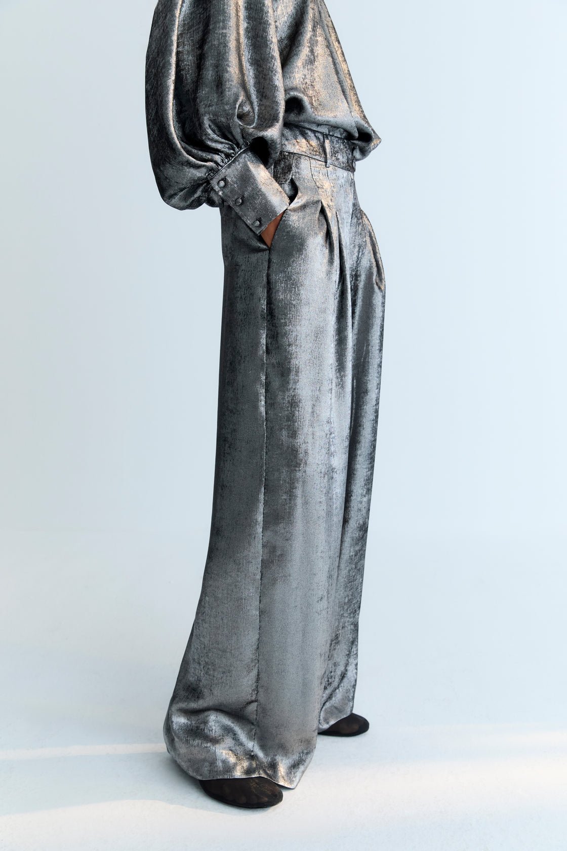Straight pants in silver shine fabric with front pleat detailing, pockets, and a crossover waistband with a hidden button.