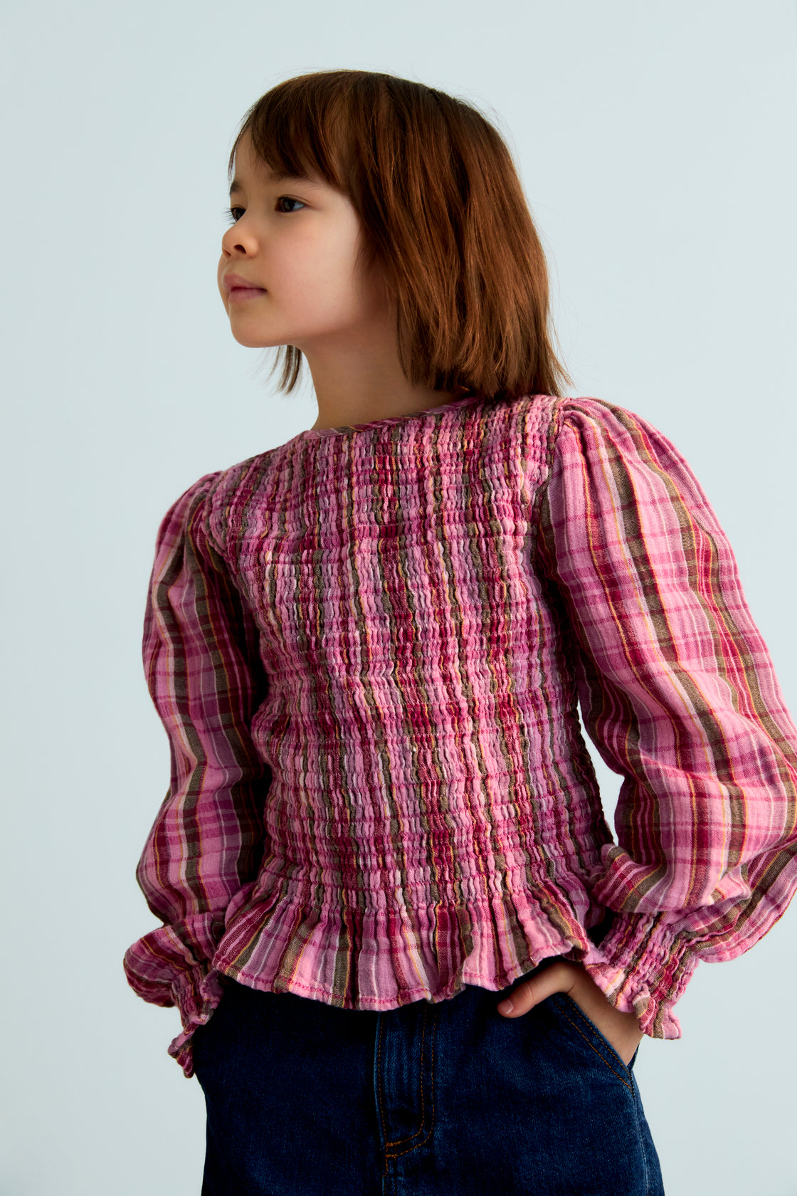 Checkered double gauze blouse with a smocked bodice and ruffle trim at the hem. It features slightly puffed sleeves and a back opening with a teardrop-shaped cut and button closure. Comes with a matching skirt to complete the look.