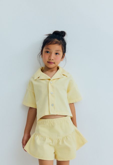 Short sleeve cropped shirt in washed denim, featuring a front snap closure, chest pocket, and TNS heart embroidery. A playful, versatile piece, perfect for completing the look with the matching shorts.